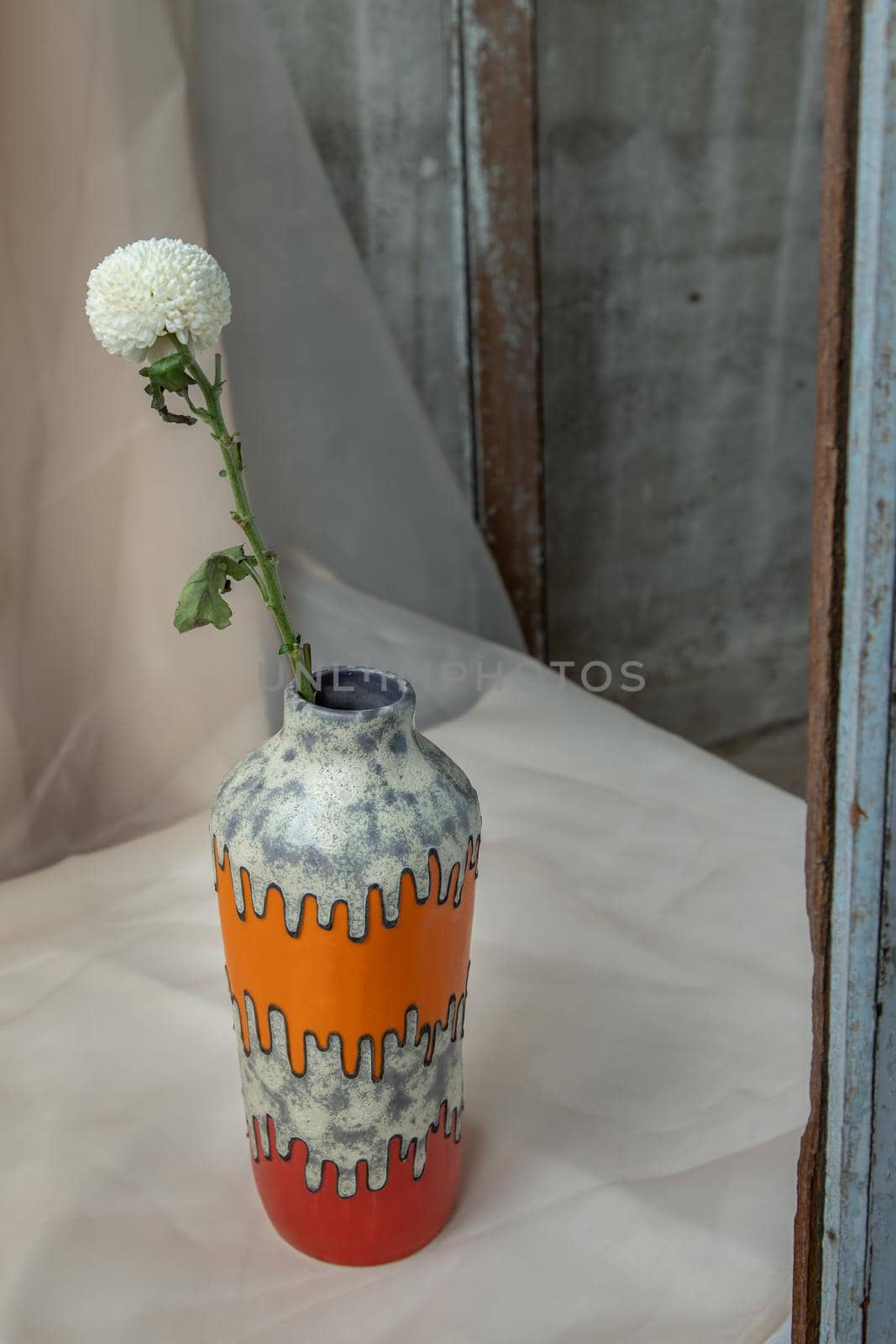 White flower in Orange and Red handmade ceramic vase on Blush textured table cloth. Home decor, Copy space, Selective focus.