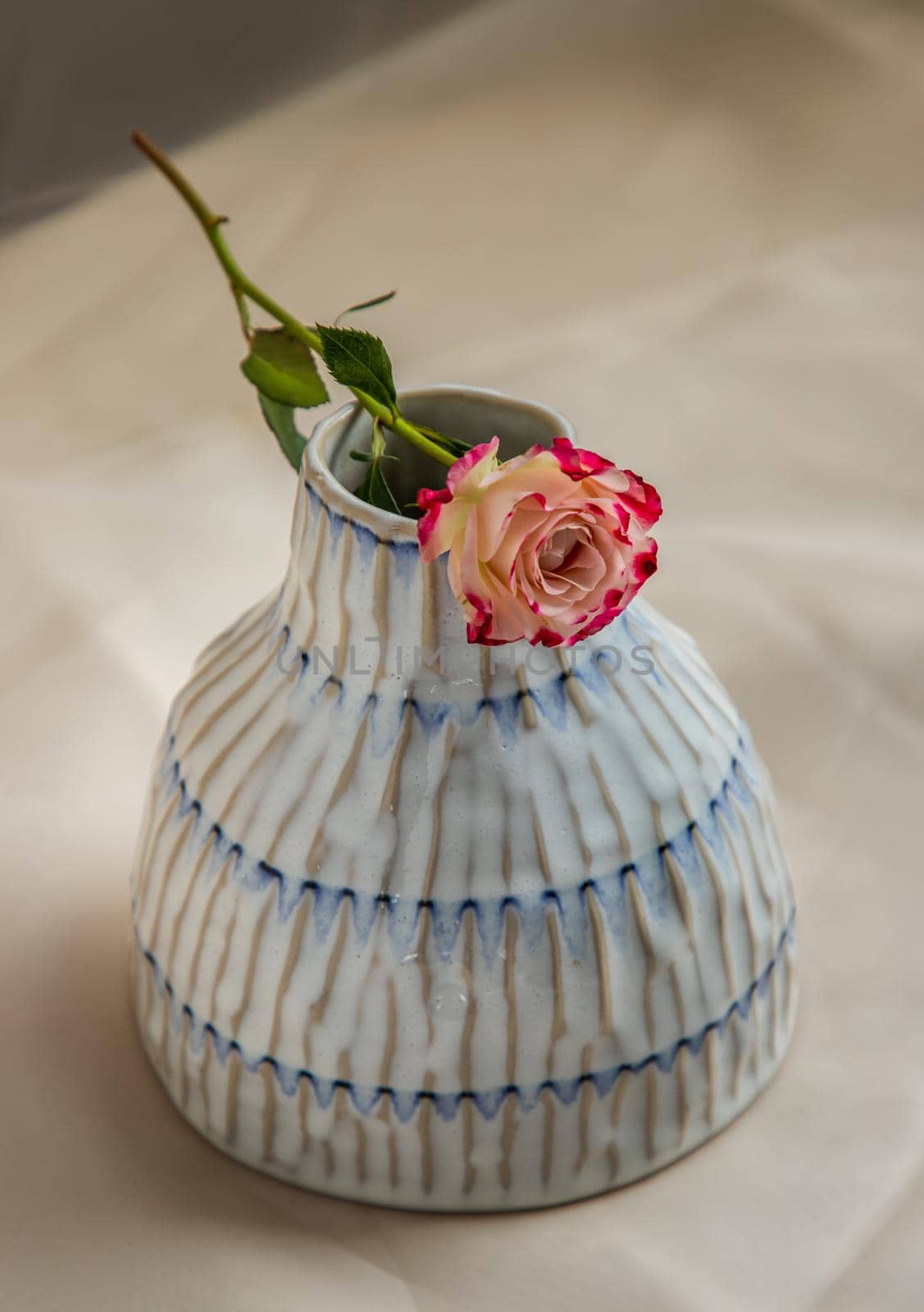 Rose flower on Copper color handmade ceramic vase and on Blush textured table cloth. Home decor, Copy space, Selective focus.