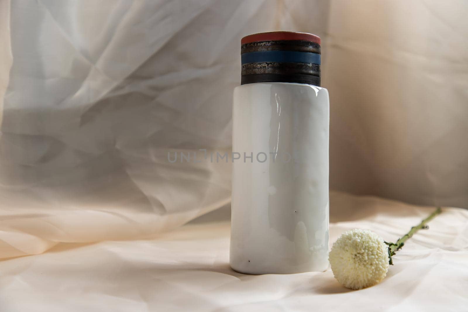 White handmade ceramic vase with White flower on Blush textured table cloth. Home decor, Copy space, Selective focus.
