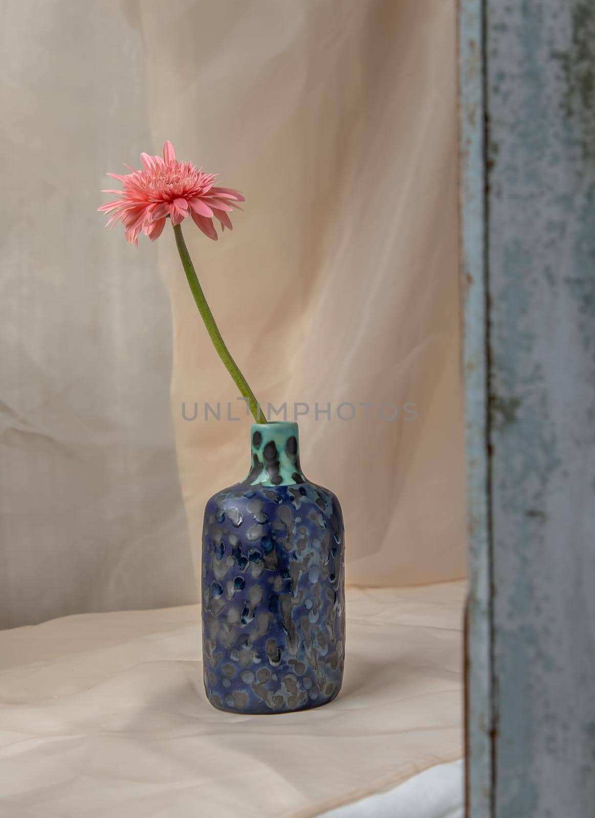Pink flower in Blue handmade ceramic vase on Blush textured table cloth. Home decor, Copy space, Selective focus.