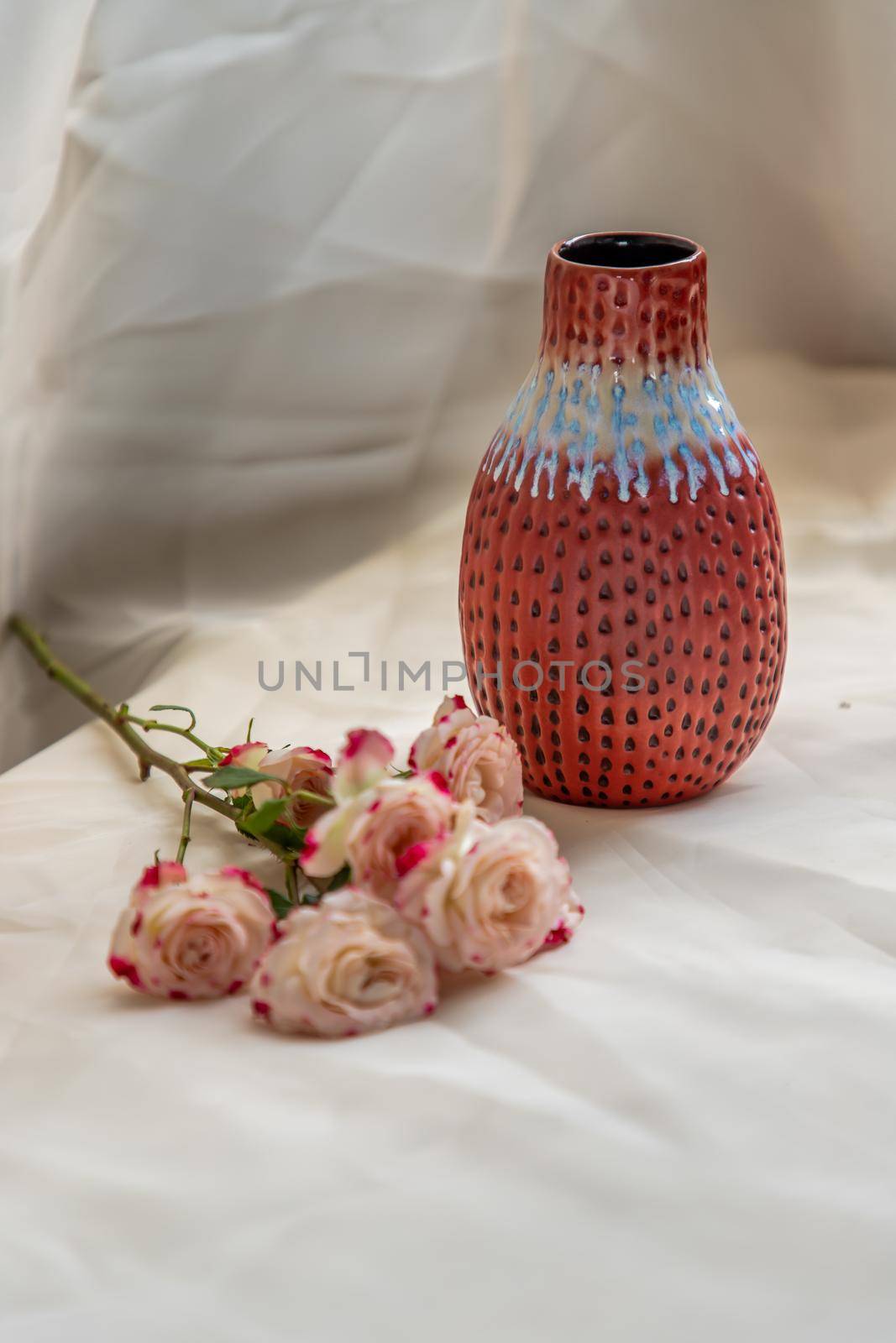 Red vase with Bouquet of flowers on Blush textured table cloth. Home decor, Copy space, Selective focus.