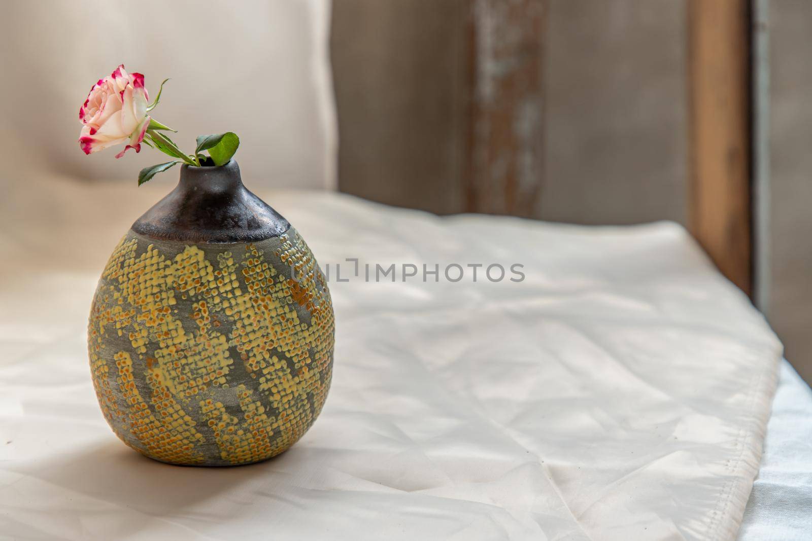 Flower in Yellow handmade ceramic vase on Blush textured table cloth. Home decor, Copy space, Selective focus.