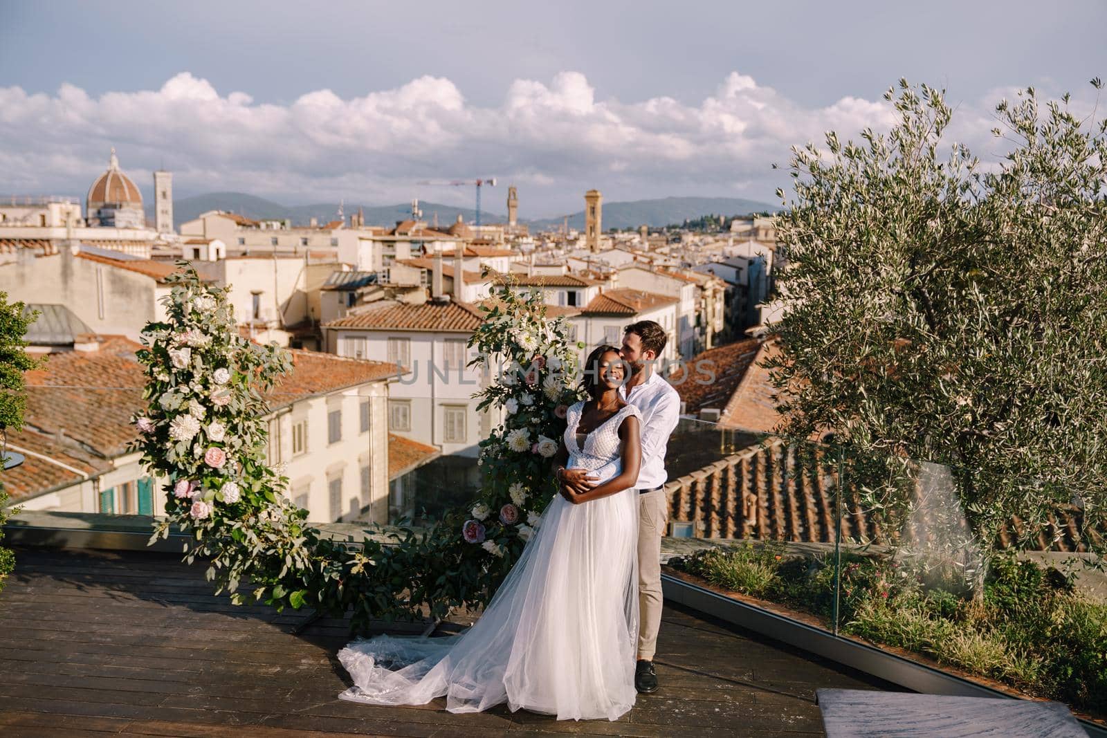 Multiethnic wedding couple. Destination fine-art wedding in Florence, Italy. A wedding ceremony on the roof of the building, with cityscape views of the city and the Cathedral of Santa Maria Del Fiore by Nadtochiy