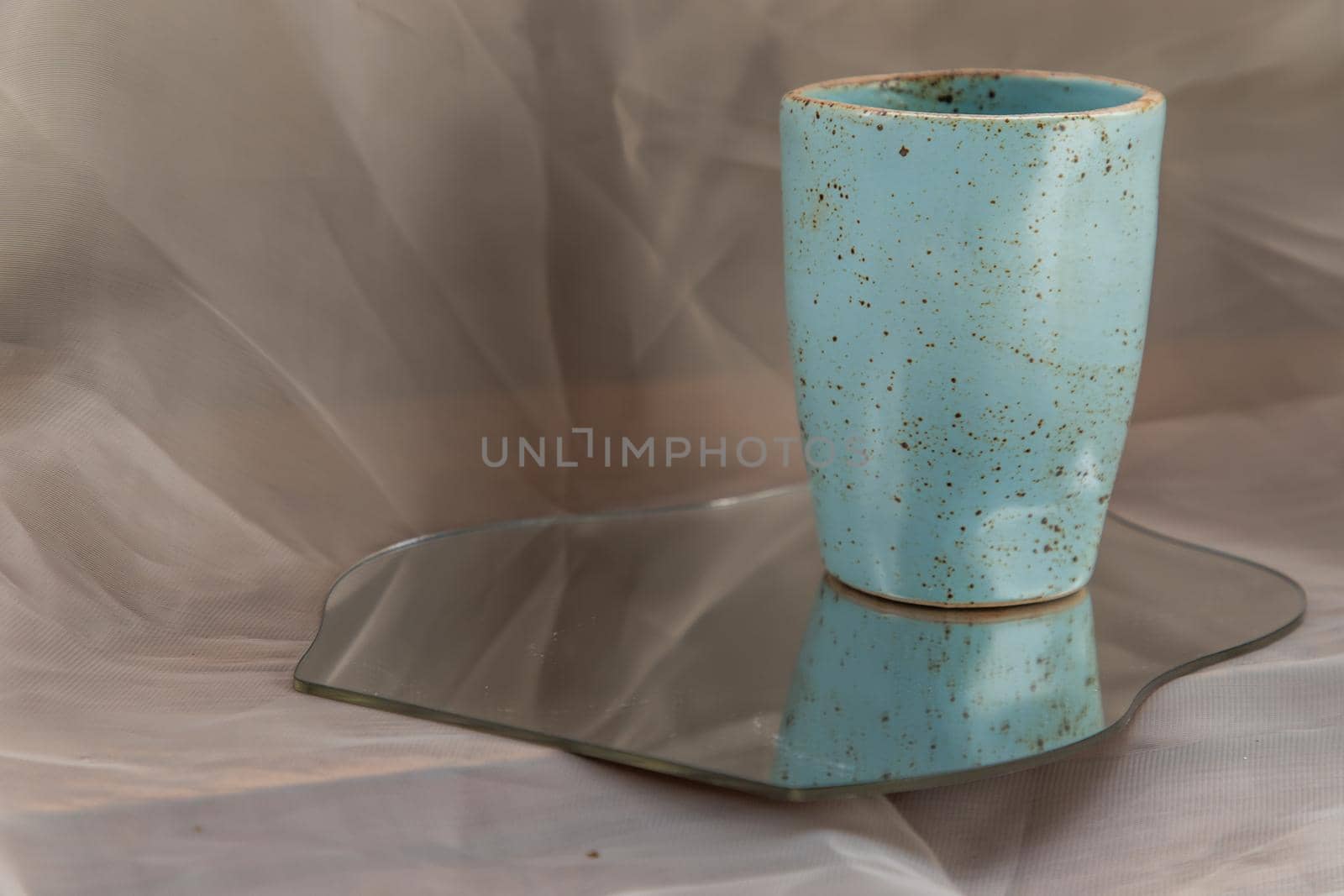 Blue handmade ceramic mug on mirror on fabric textured table cloth. Home decor, Copy space, Selective focus.
