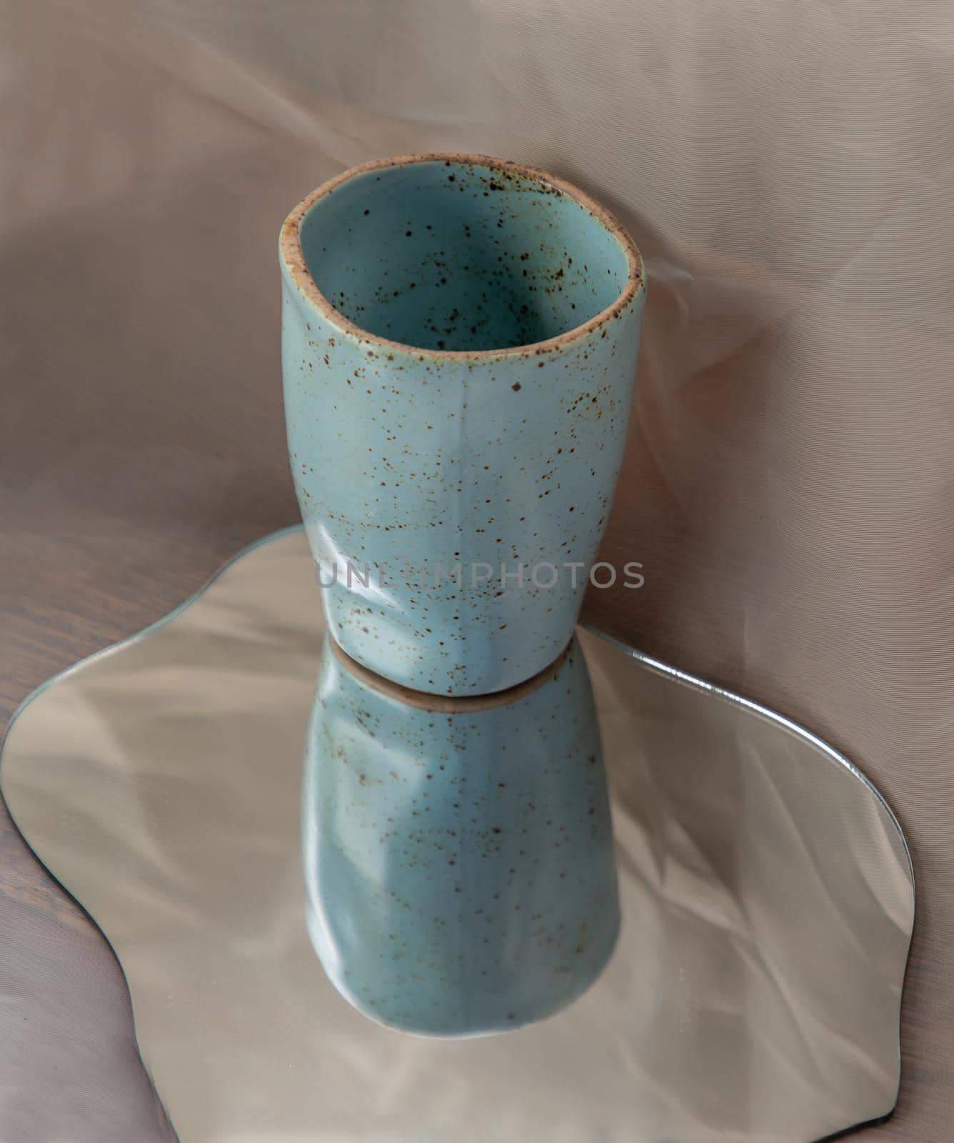 Blue handmade ceramic mug on mirror on fabric textured table cloth. Home decor, Copy space, Selective focus.