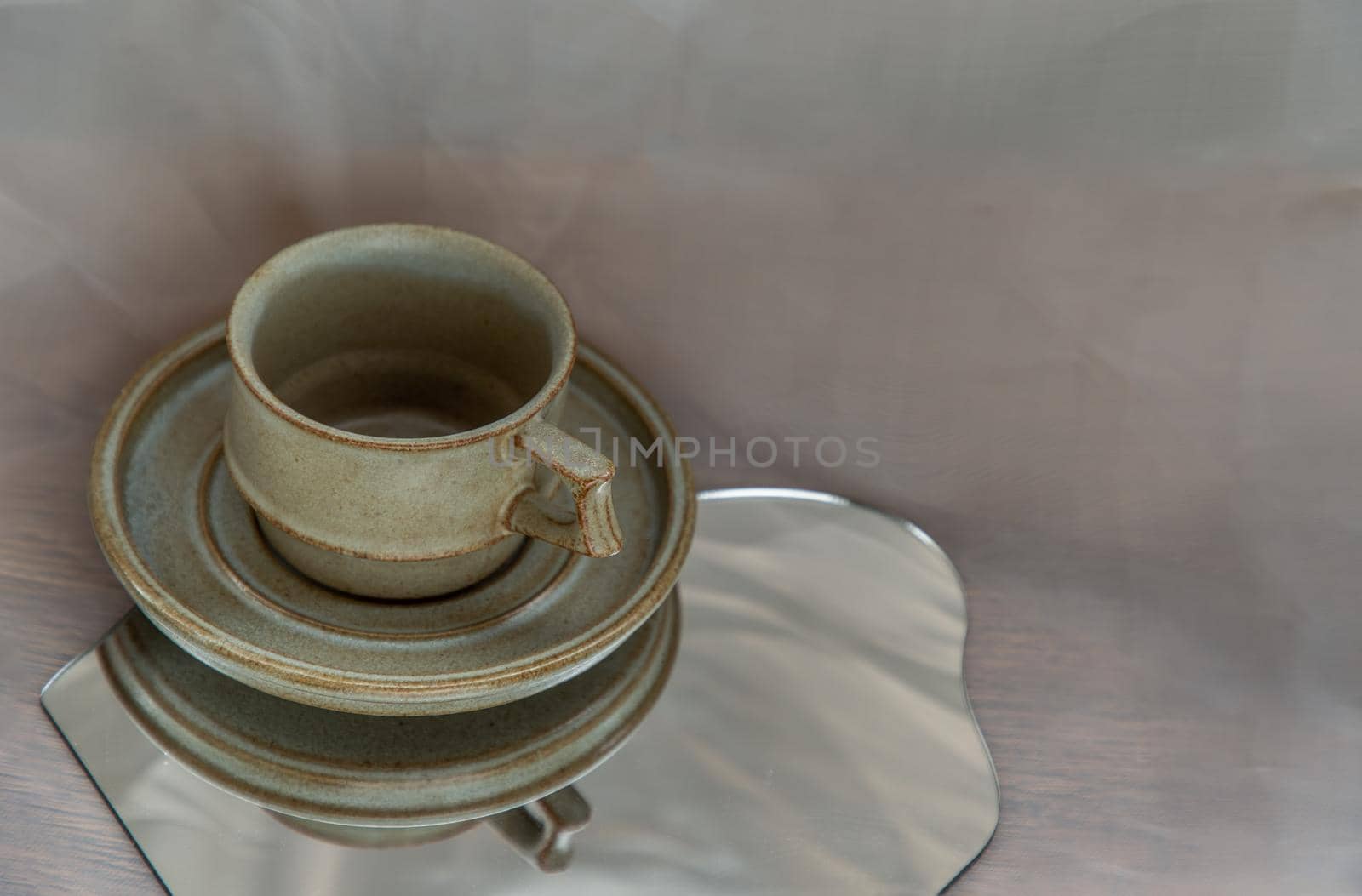 Handmade ceramic coffee mug on mirror on fabric textured table cloth. Home decor, Copy space, Selective focus.