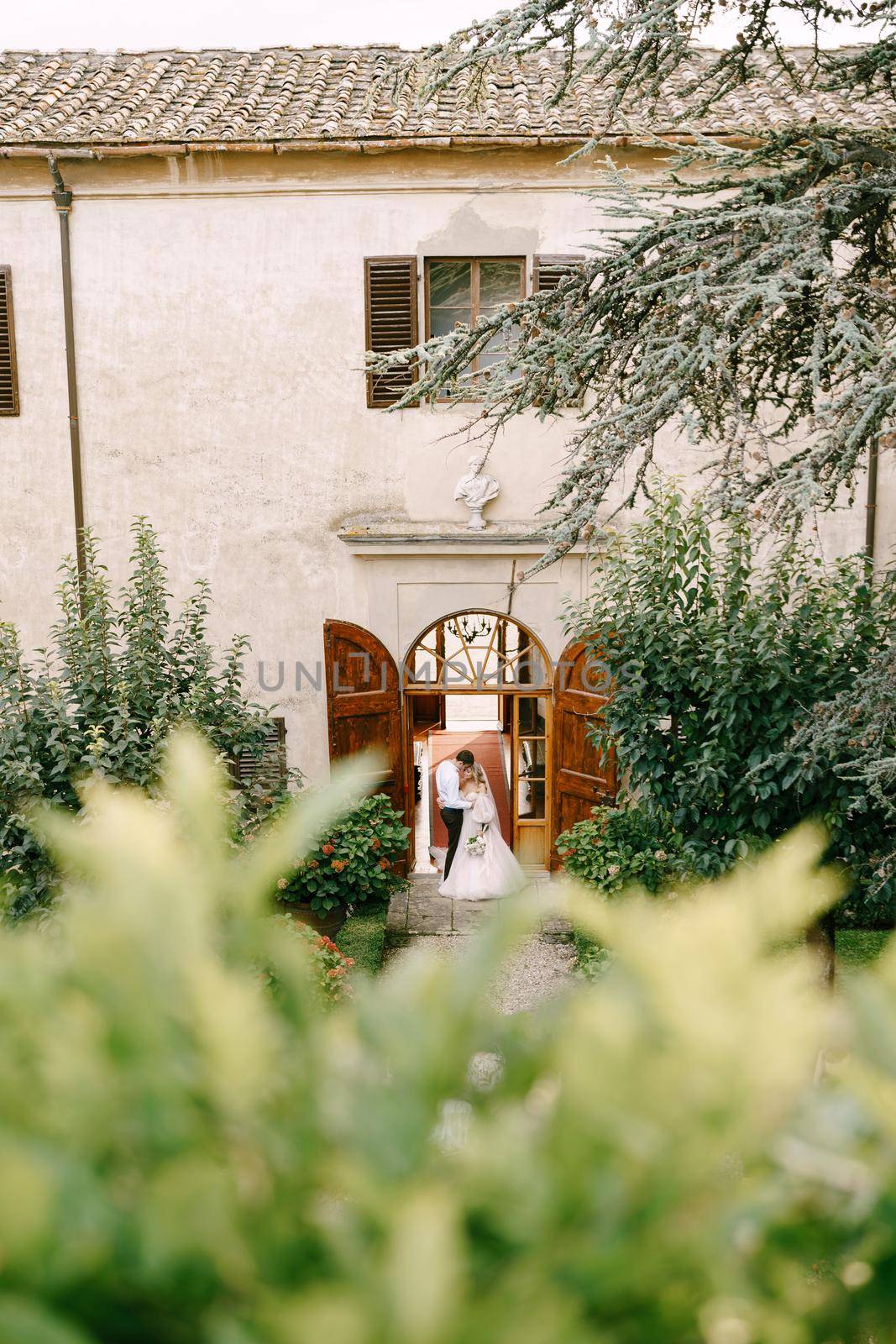 Wedding at an old winery villa in Tuscany, Italy. A wedding couple stands near the old wooden doors at the villa-winery.