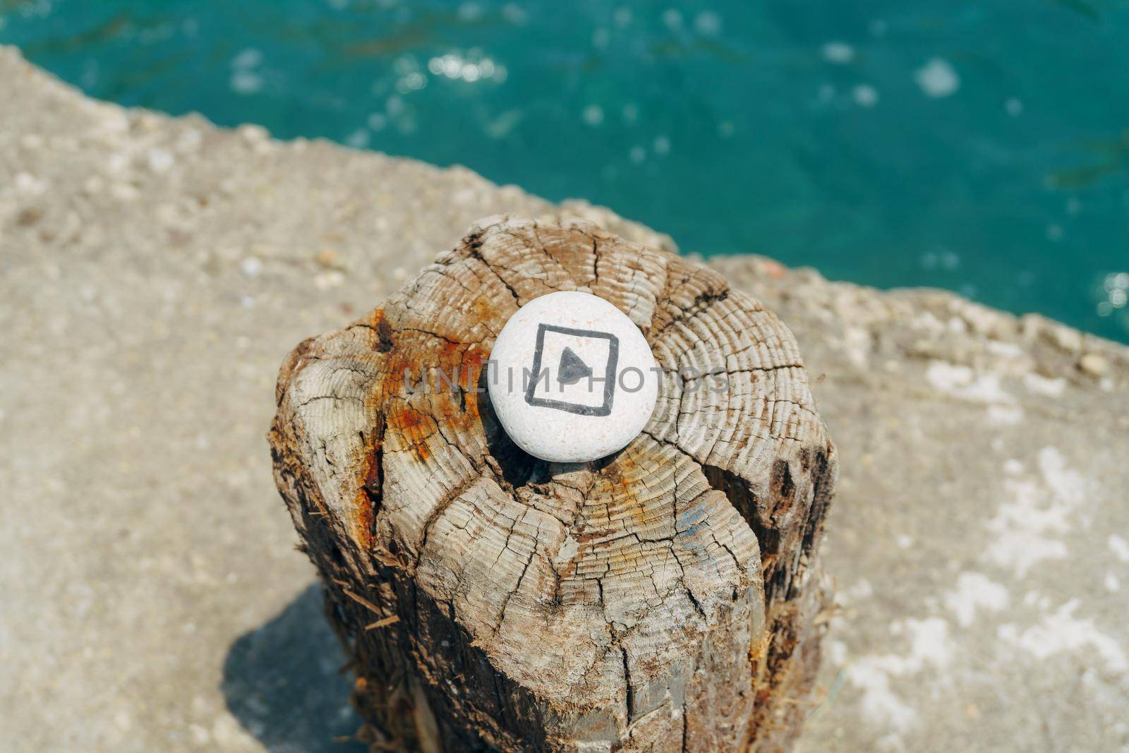 The play sign painted on the sea pebble, lies on the stump, against the sea
