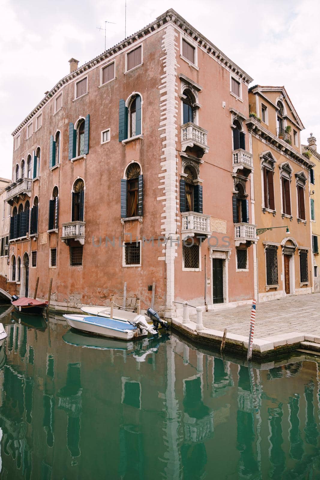 A wide frame of the corner of the three-story house, peach-colored, near a small narrow Venetian Canal. A motorboat moored near the walls of a house standing in the water in Venice, Italy.