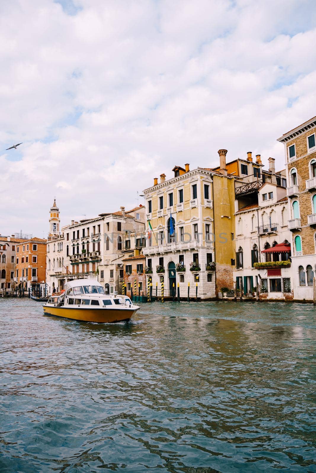 Tourists on the waterfront in Venice, against the background of the ancient facades of buildings standing in water. Water sightseeing in Venice, Italy.