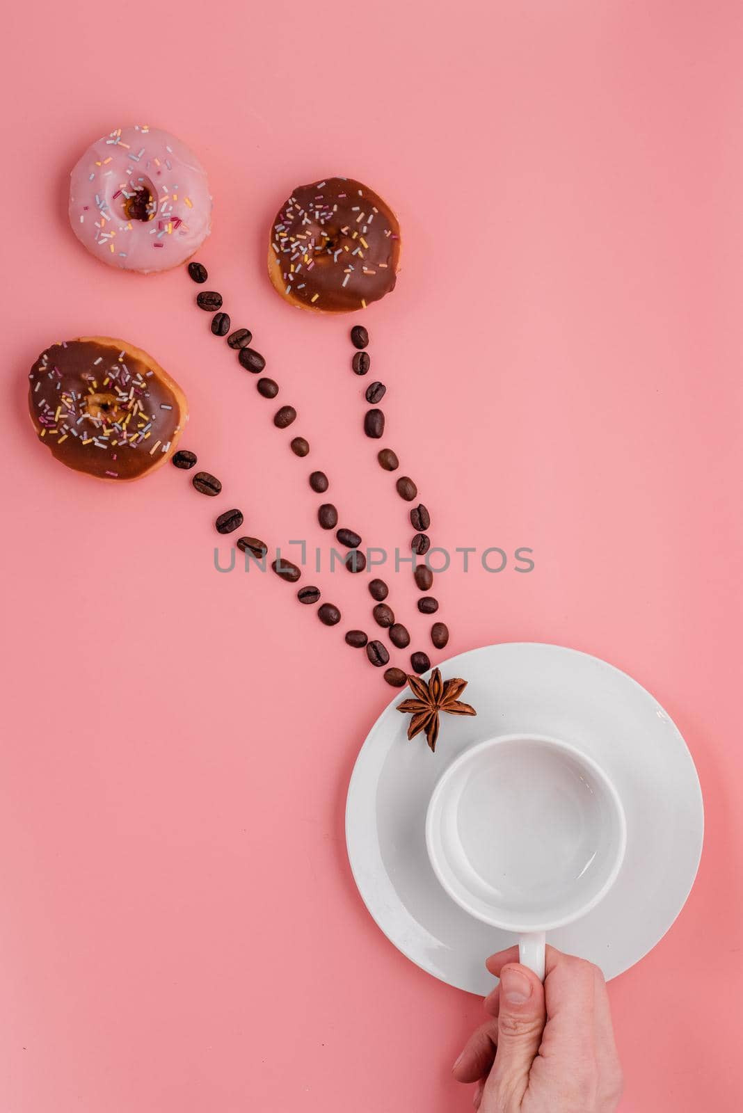 hand holding empty cup, beans and three doughnut on pink background