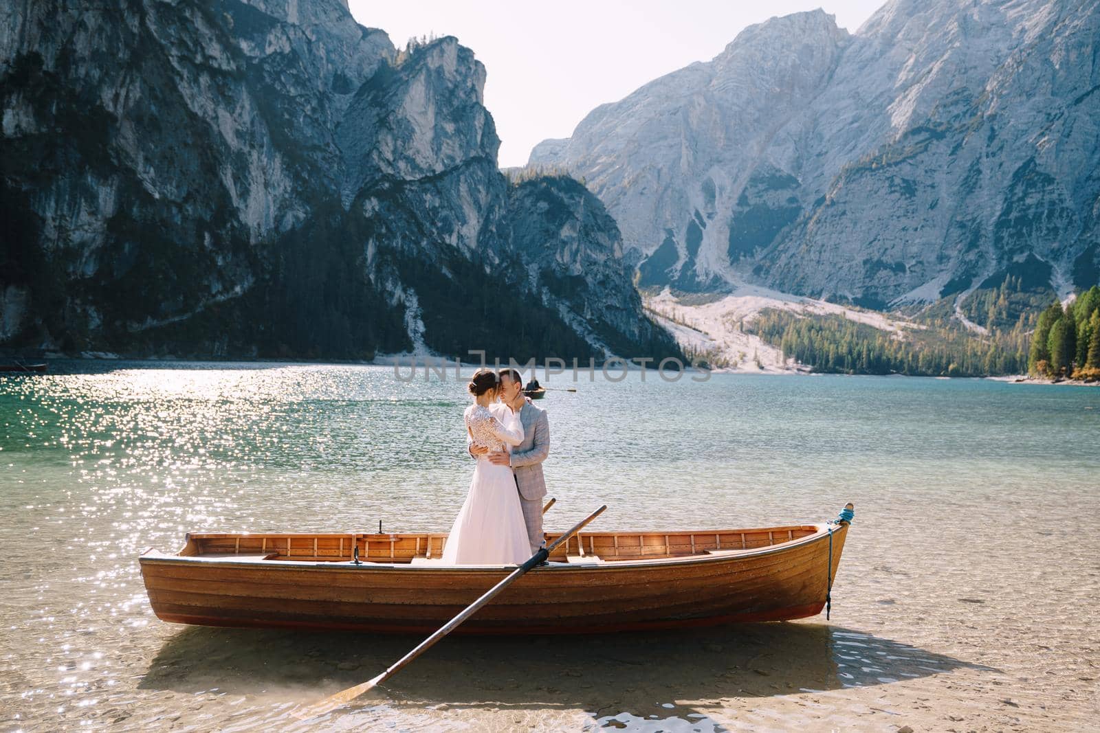 Bride and groom sailing in wooden boat, with oars at Lago di Braies lake in Italy. Wedding in Europe - Newlyweds are standing embracing in boat