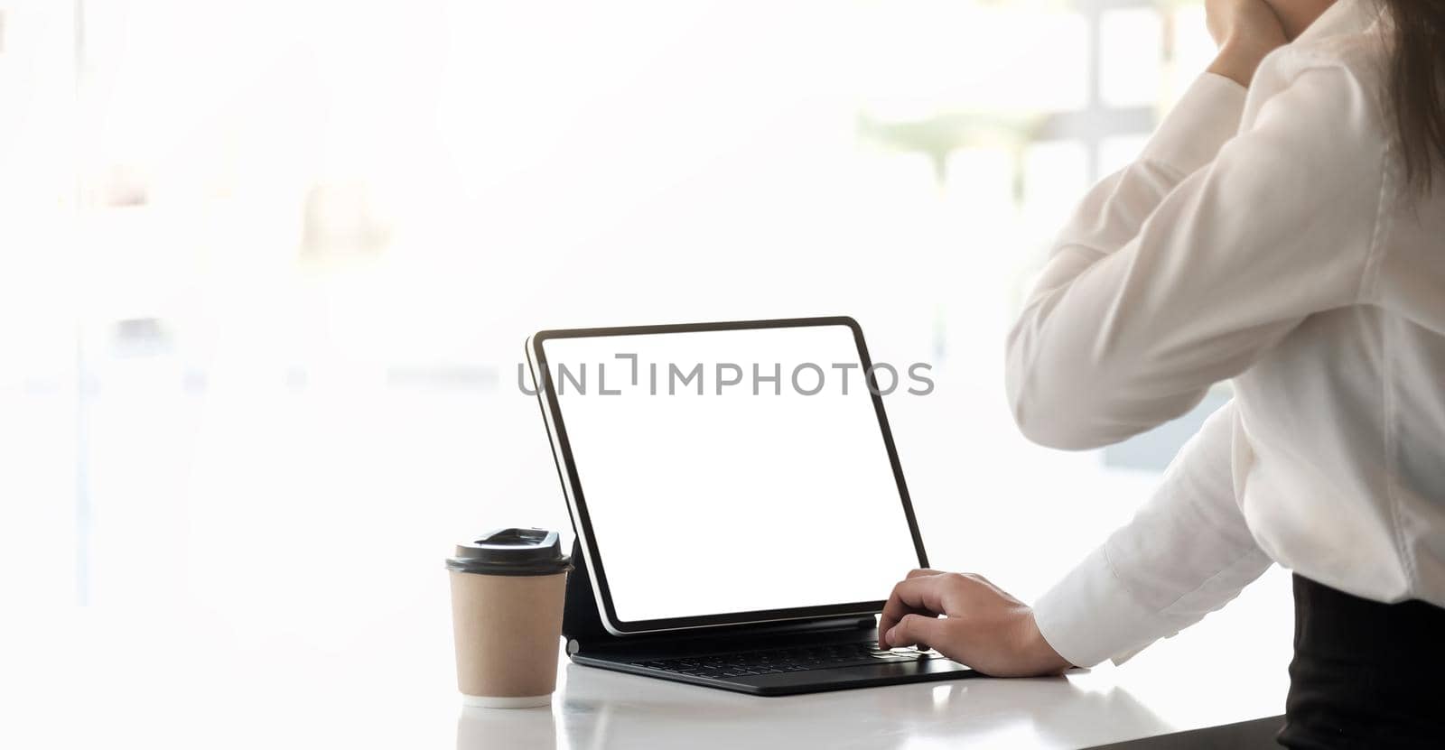 Sleepy young woman dressed in shirt sitting at her workplace typing smart tablet blank screen.