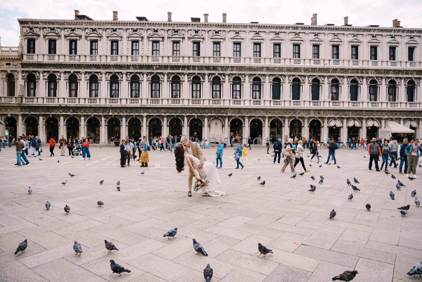 Venice, Italy - 04 october 2019: Wedding in Venice, Italy. The bride and groom kiss among the many pigeons in Piazza San Marco, against the backdrop of the National Archaeological Museum Venice by Nadtochiy