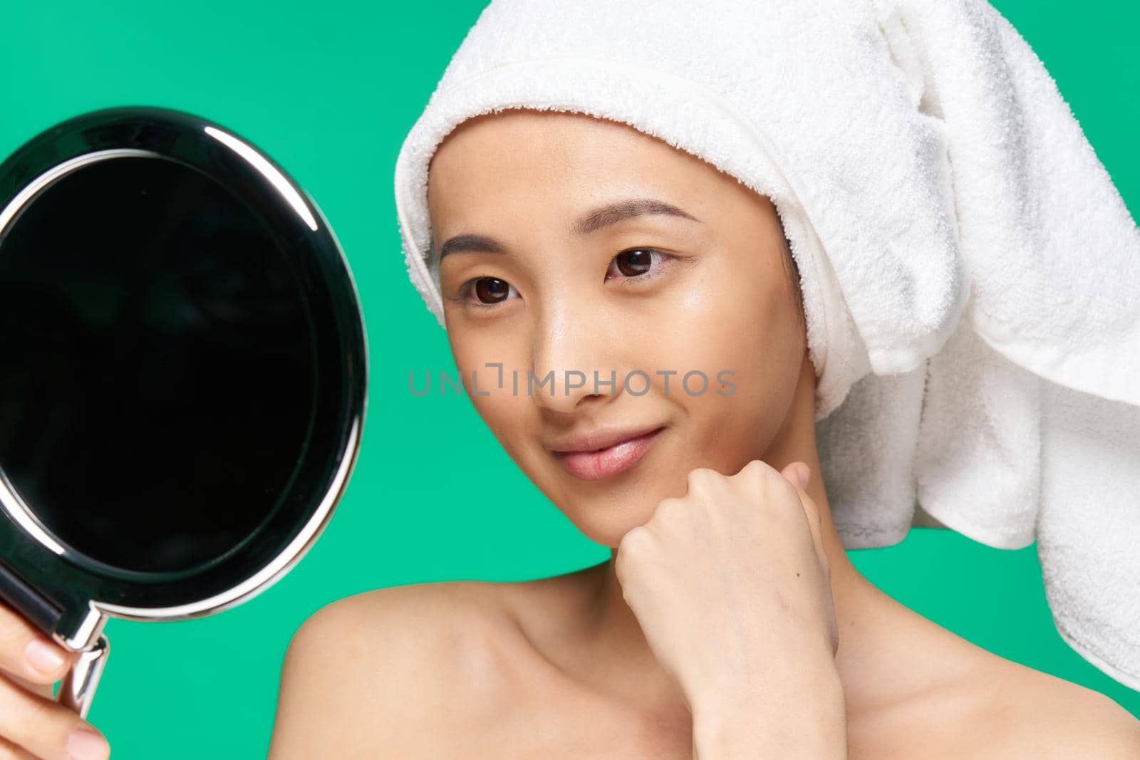 woman of asian appearance looks mirrors clean skin green background hand near face. High quality photo