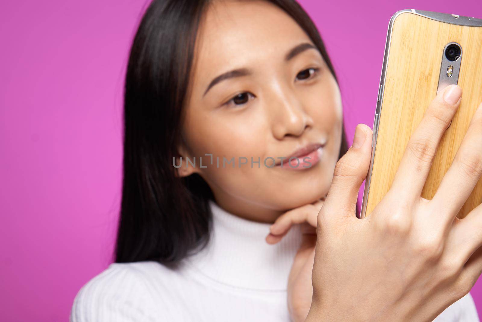 woman asian appearance phone in hands close-up technology gadget pink background. High quality photo