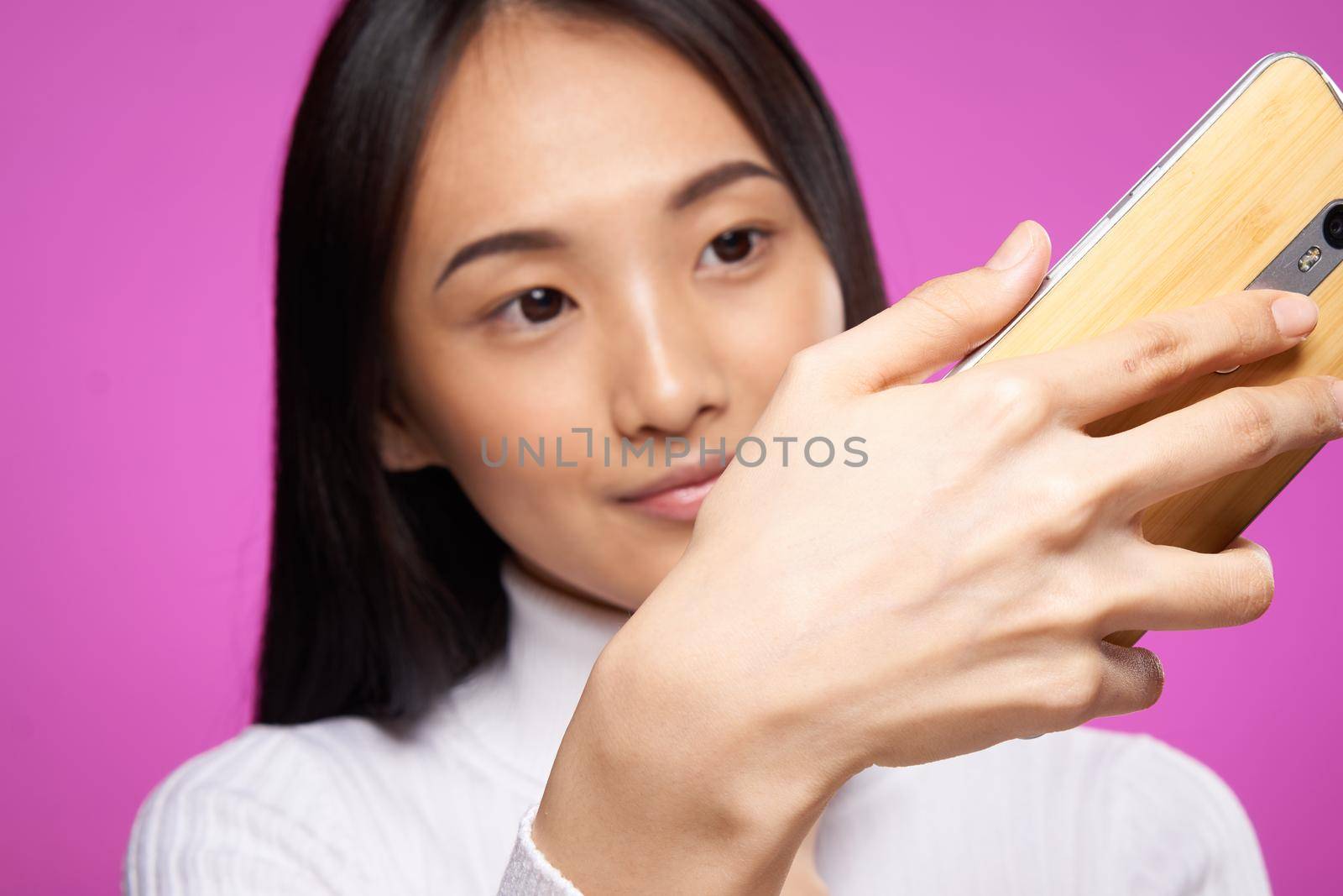 woman asian appearance phone in hands close-up technology gadget pink background. High quality photo