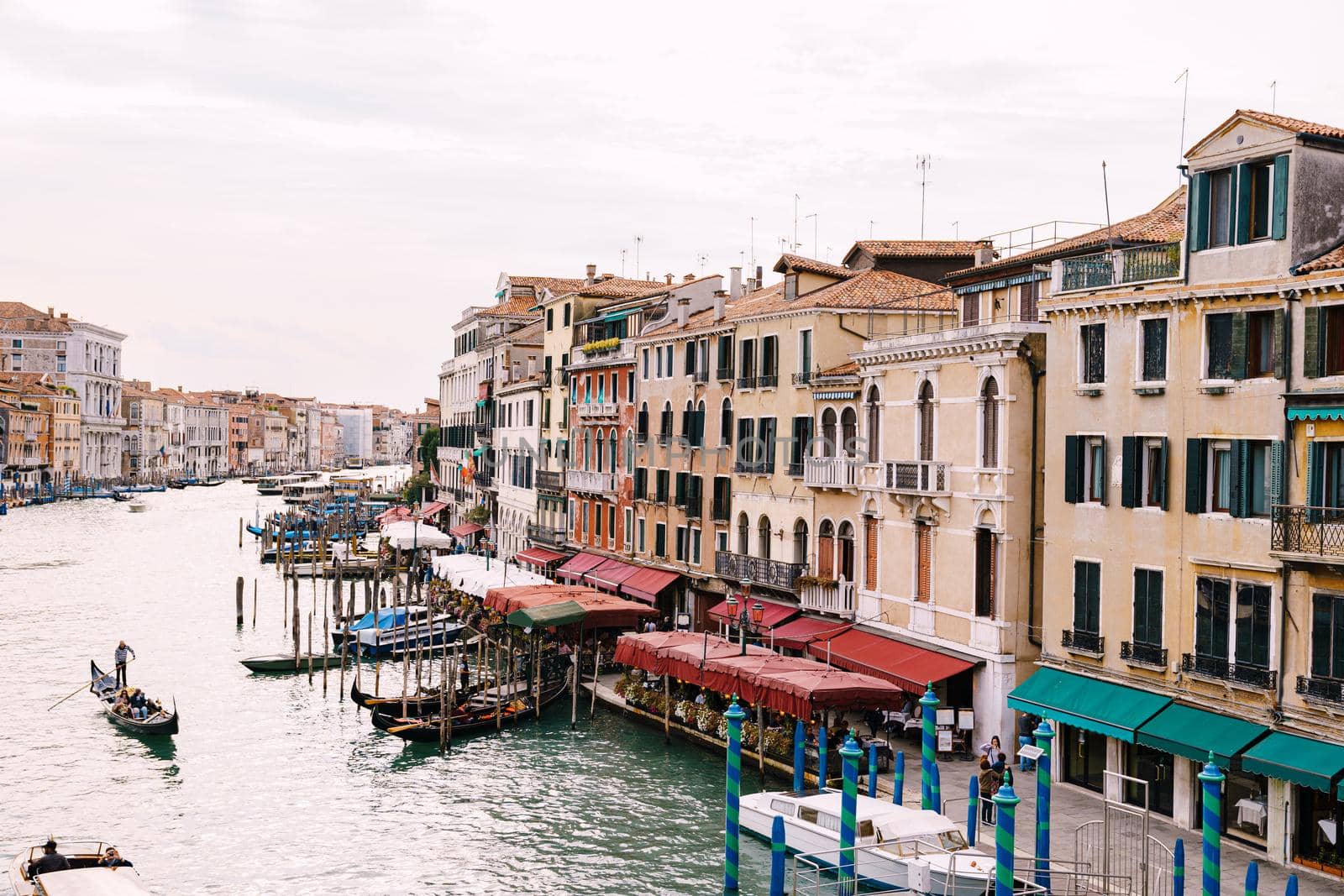 Grand Canal Embankment in Venice, Italy. Near the Rialto Bridge. People ride beautiful wooden motor boats, gondoliers carry tourists, large ships with people stand at the pier.