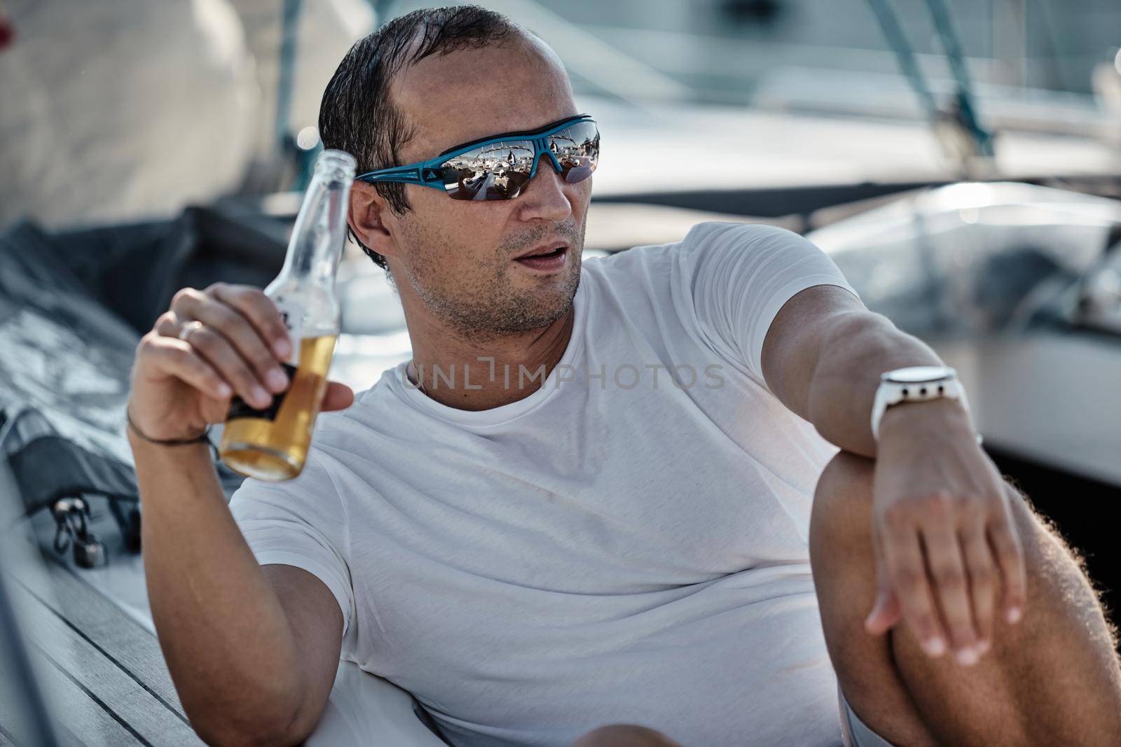 Croatia, Split, 15 September 2019: Brutal participant of a sailing regatta with boats on a background is waiting for the forthcoming race, he drinks a beer, skiper or sailor, sunglasses by vladimirdrozdin