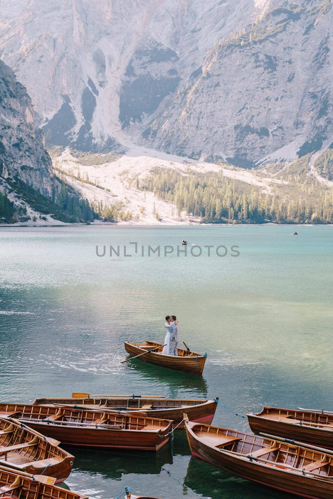 Bride and groom sailing in wooden boat, with oars at Lago di Braies lake in Italy. Wedding in Europe - Newlyweds are standing embracing in a boat. by Nadtochiy