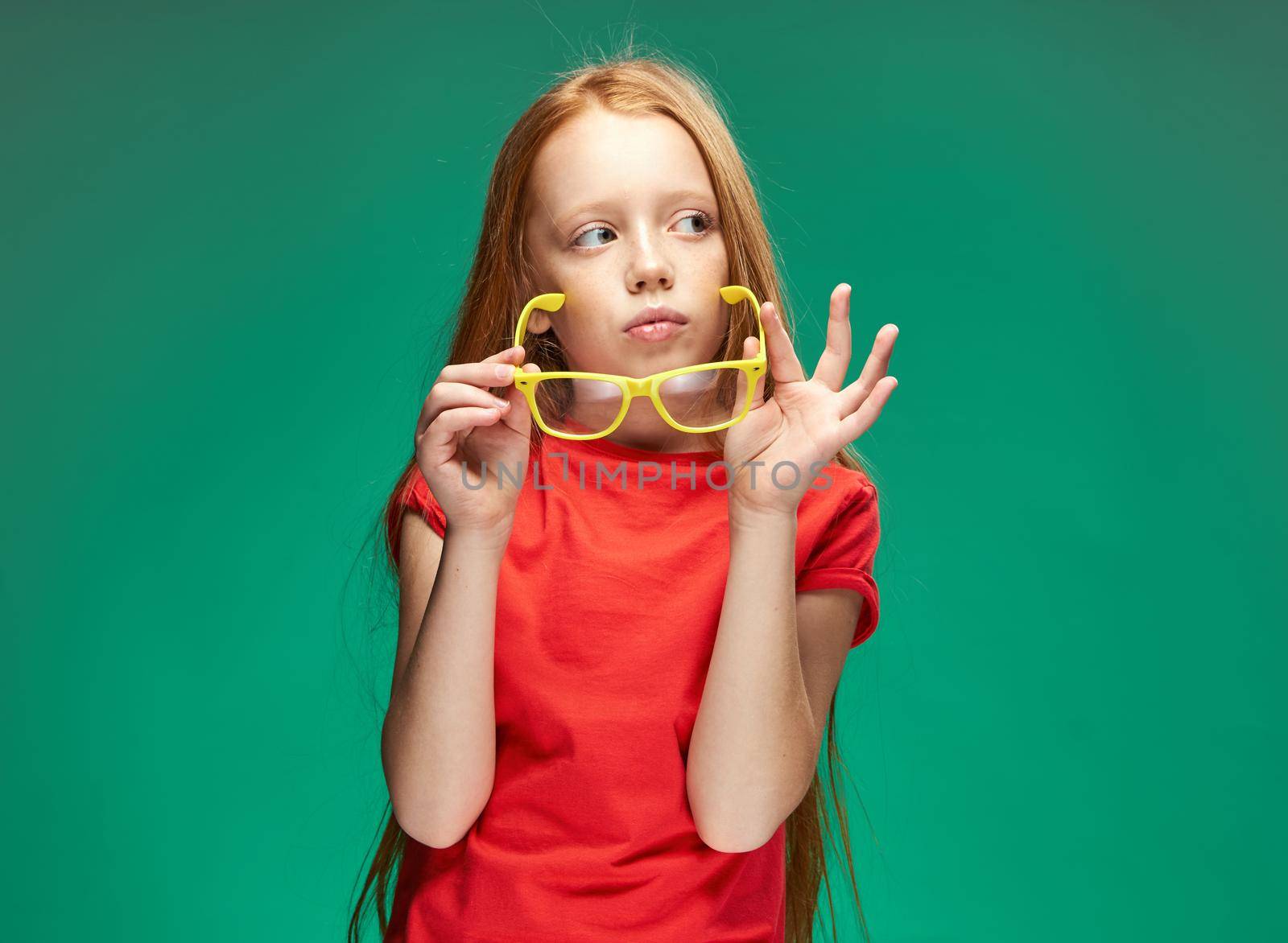 cheerful red-haired girl holding glasses in her hands learning school green background. High quality photo