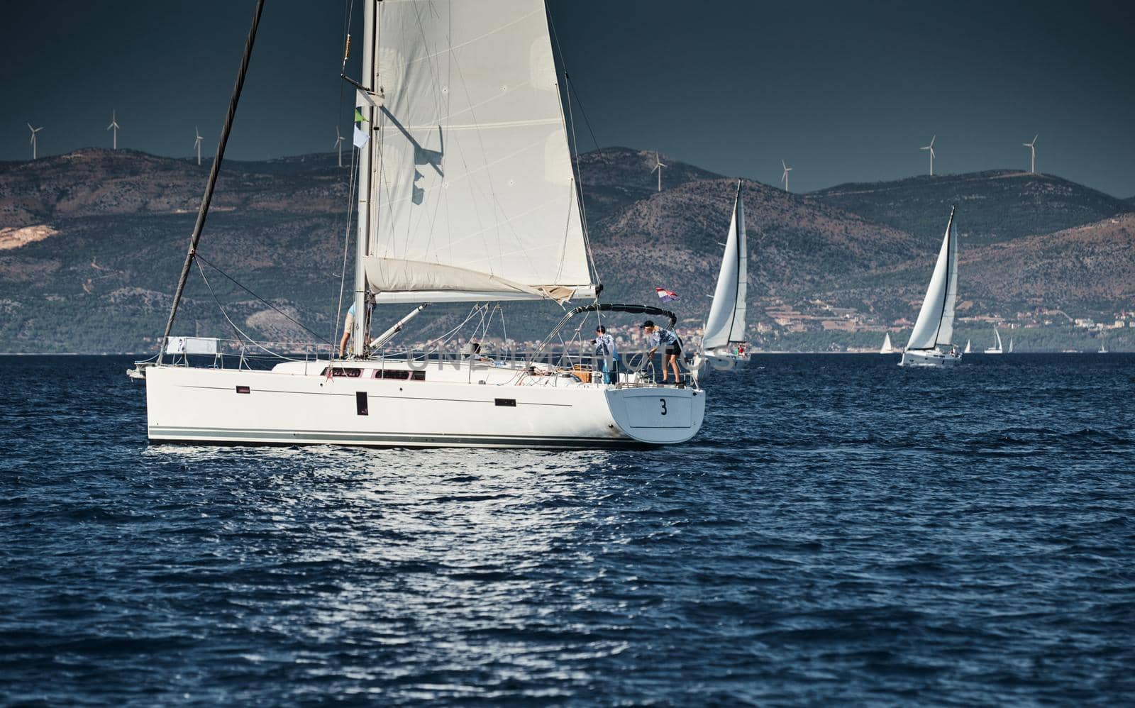 Croatia, Adriatic Sea, 15 September 2019: The race of sailboats, a regatta, reflection of sails on water, Intense competition, bright colors, island with windmills are on background by vladimirdrozdin