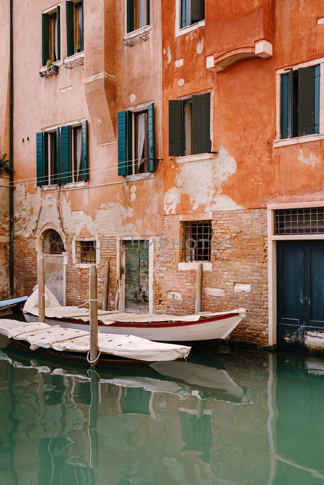Boats moored at the walls of a building in canal in Venice, Italy. Classic Venetian street views - wooden shutters, brick houses, bridges
