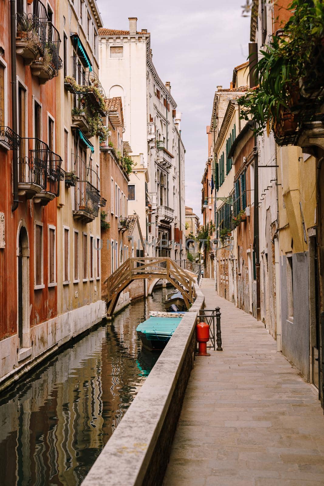 Beautiful narrow canal in Venice, Italy. Small stone bridge connects houses from both sides of the canal. Building facades are aged by weather and water.