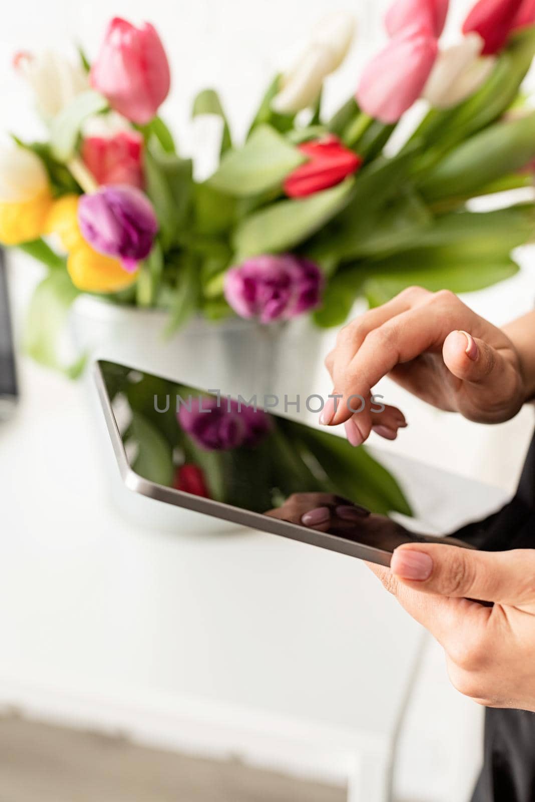 Small business concept. woman hands working on digital tablet, bucket of fresh tulips on background