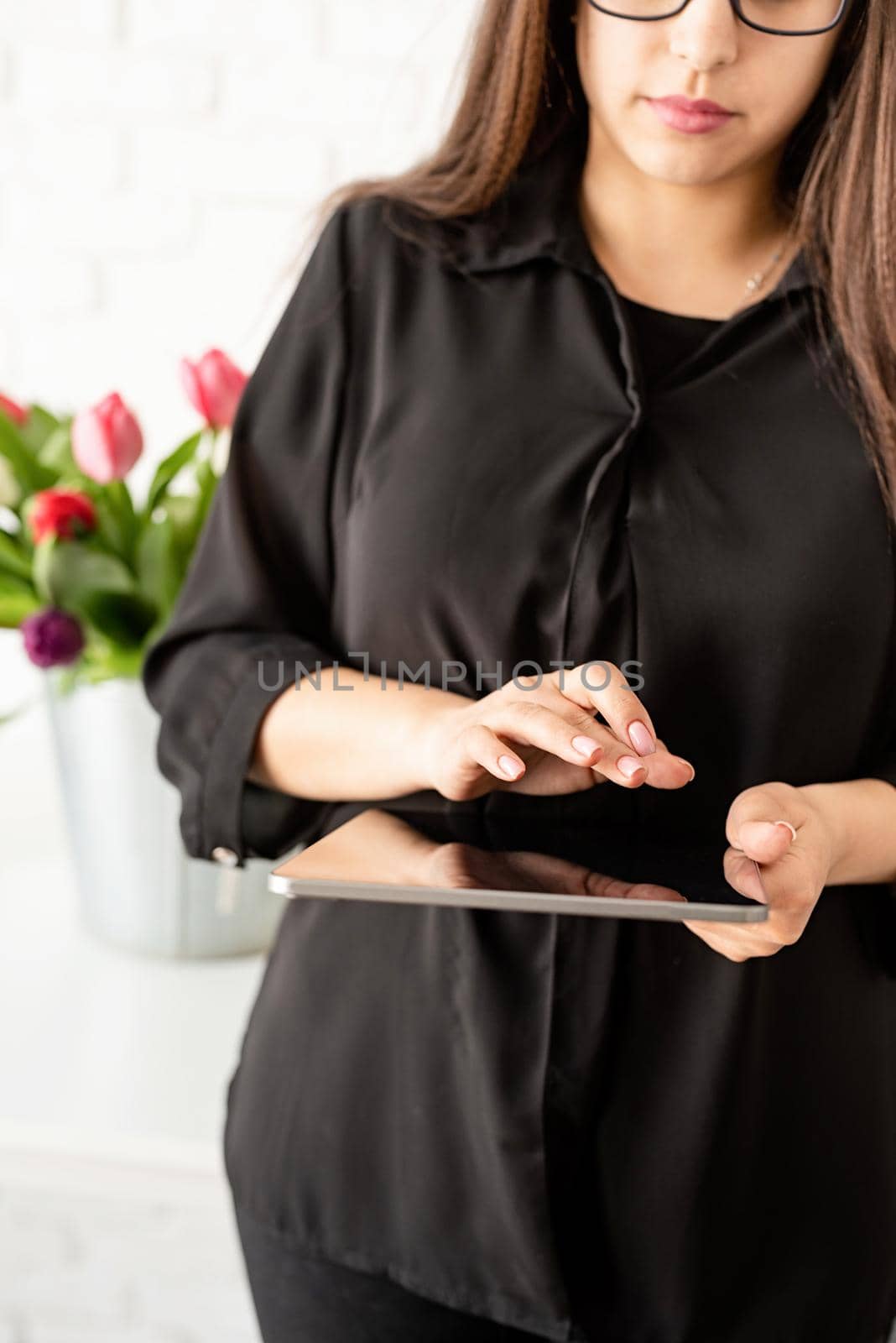 Small business concept. woman hands working on digital tablet, bucket of fresh tulips on background