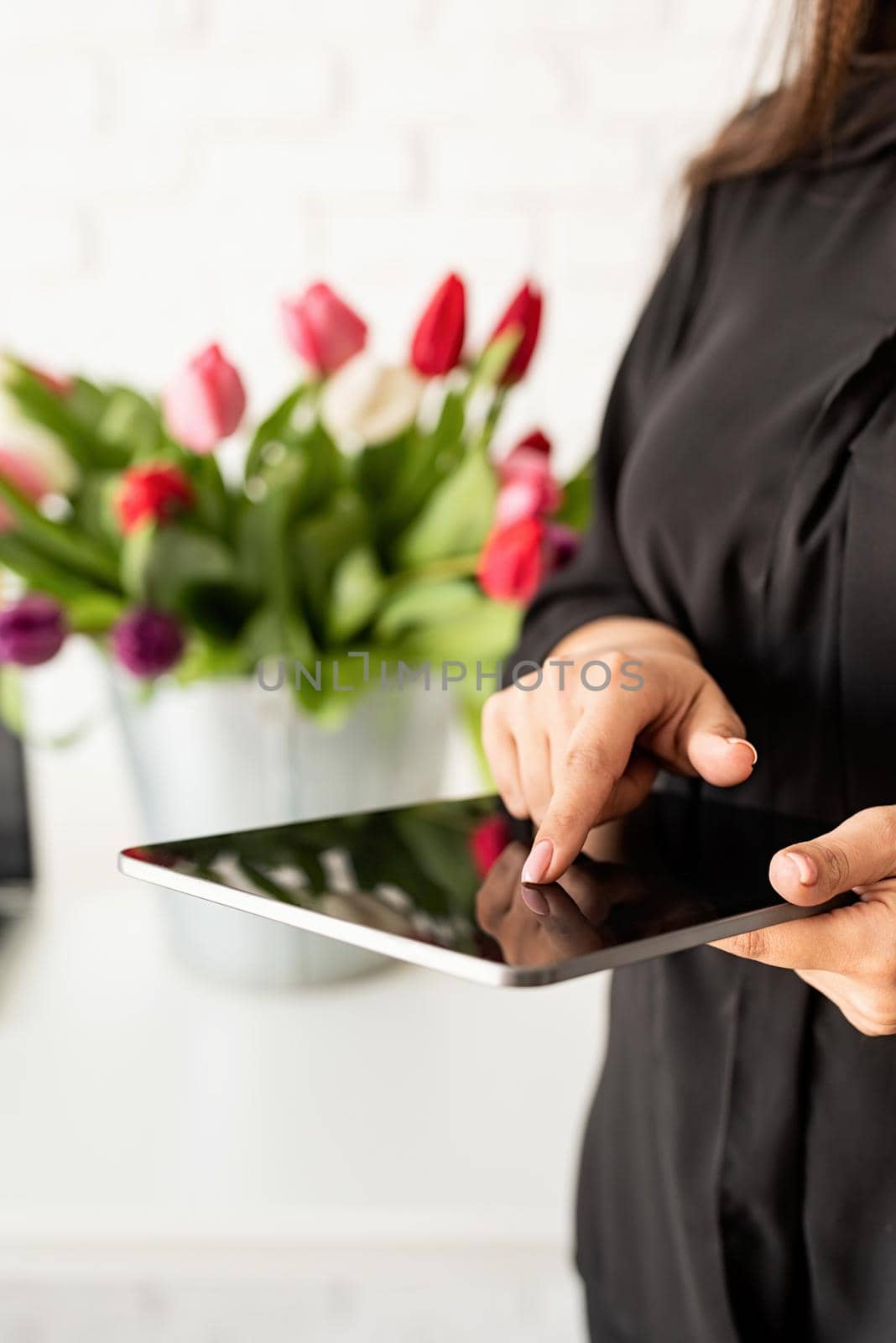 Small business concept. woman hands working on digital tablet, bucket of fresh tulips on background