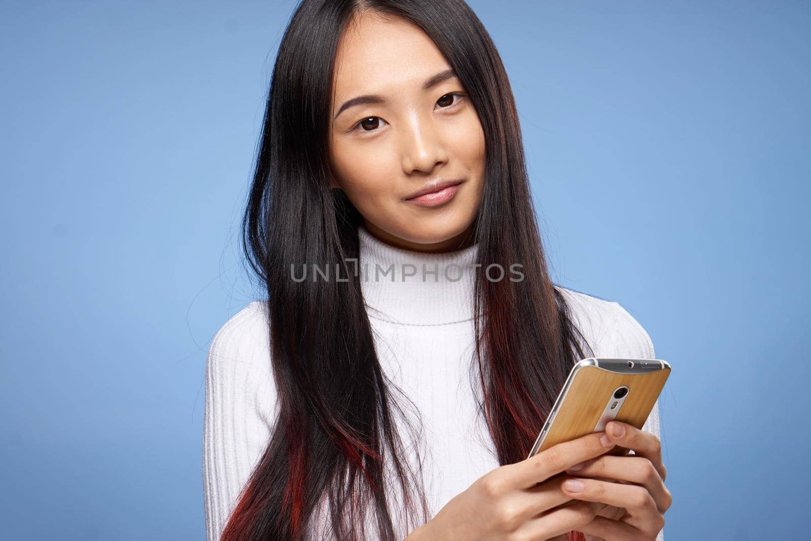 pretty brunette with phone in hands white sweater communication technology blue background. High quality photo