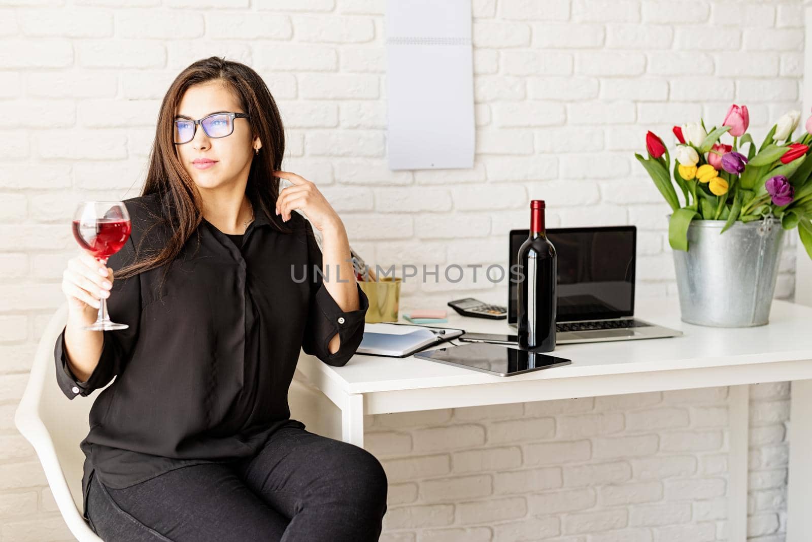 Young confident business woman drinking wine, celebrating at the office by Desperada