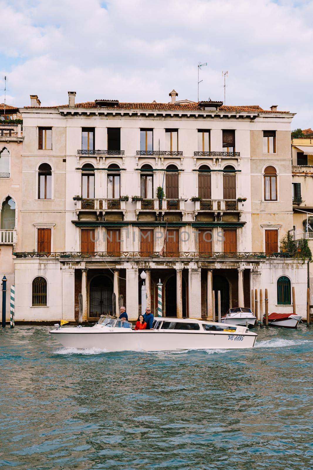 Tourists on the waterfront in Venice, against the background of the ancient facades of buildings standing in water. Water sightseeing in Venice, Italy.