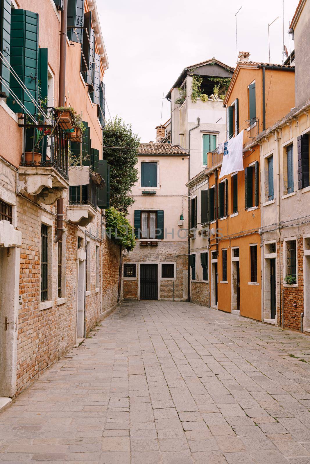 Dead end Venetian street. Five-story houses with blue-green wooden shutters on the windows, linen is dried in the windows, an old stone floor.