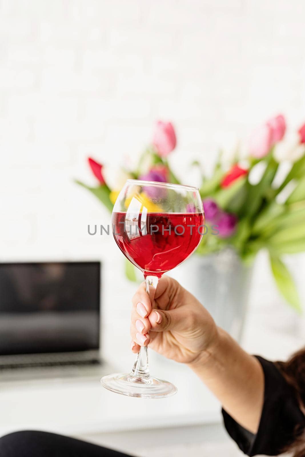 woman hand holding a glass of red wine celebrating spring holidays, bucket of tulips on background