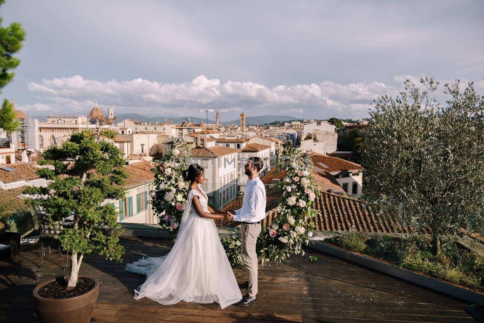 Destination fine-art wedding in Florence, Italy. Multiethnic wedding couple. A wedding ceremony on the roof of the building, with cityscape views of the city and the Cathedral of Santa Maria Del Fiore by Nadtochiy