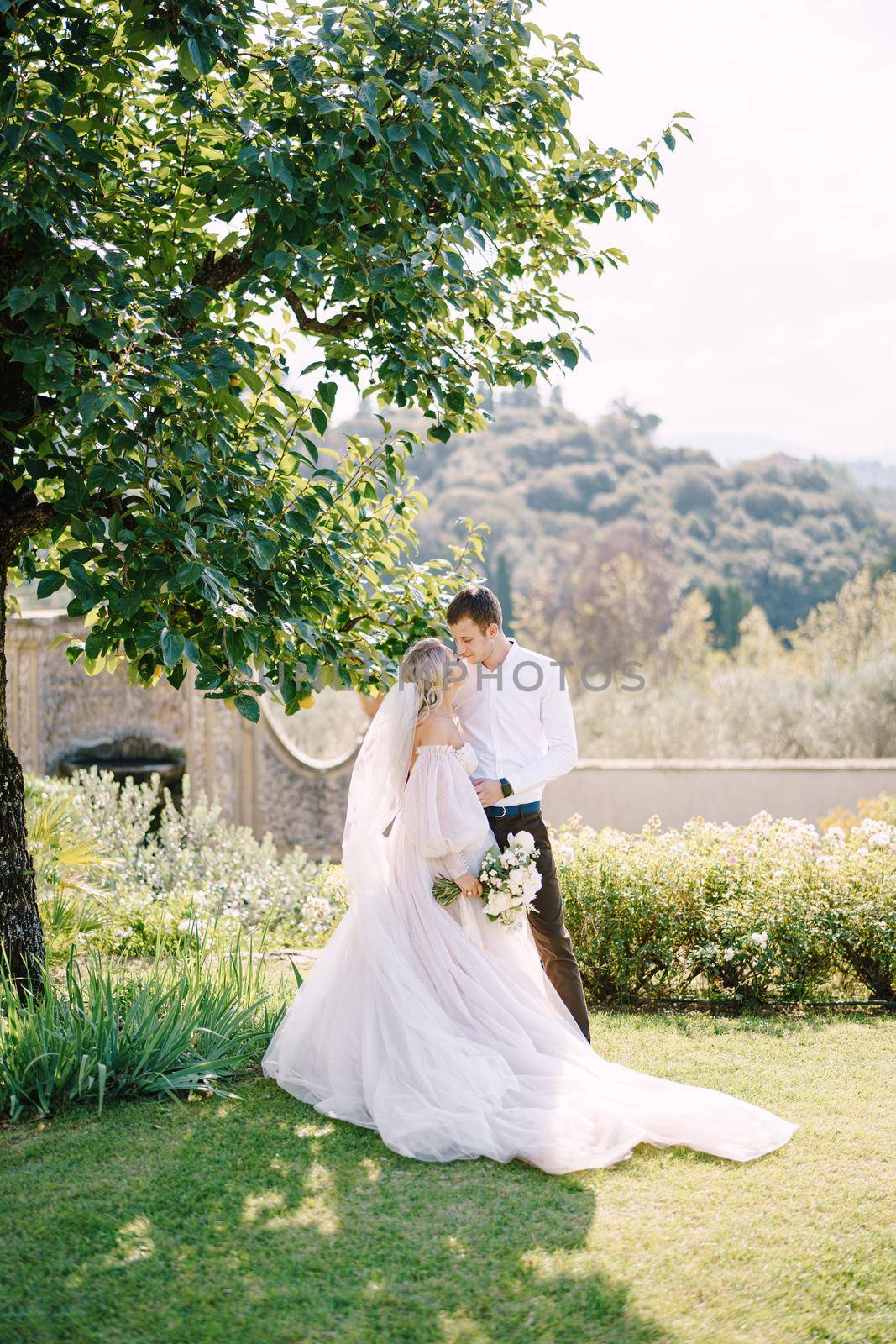 The bride and groom in the shade of a tree. The wedding couple walks in the garden. Wedding in Florence, Italy, in an old villa-winery.