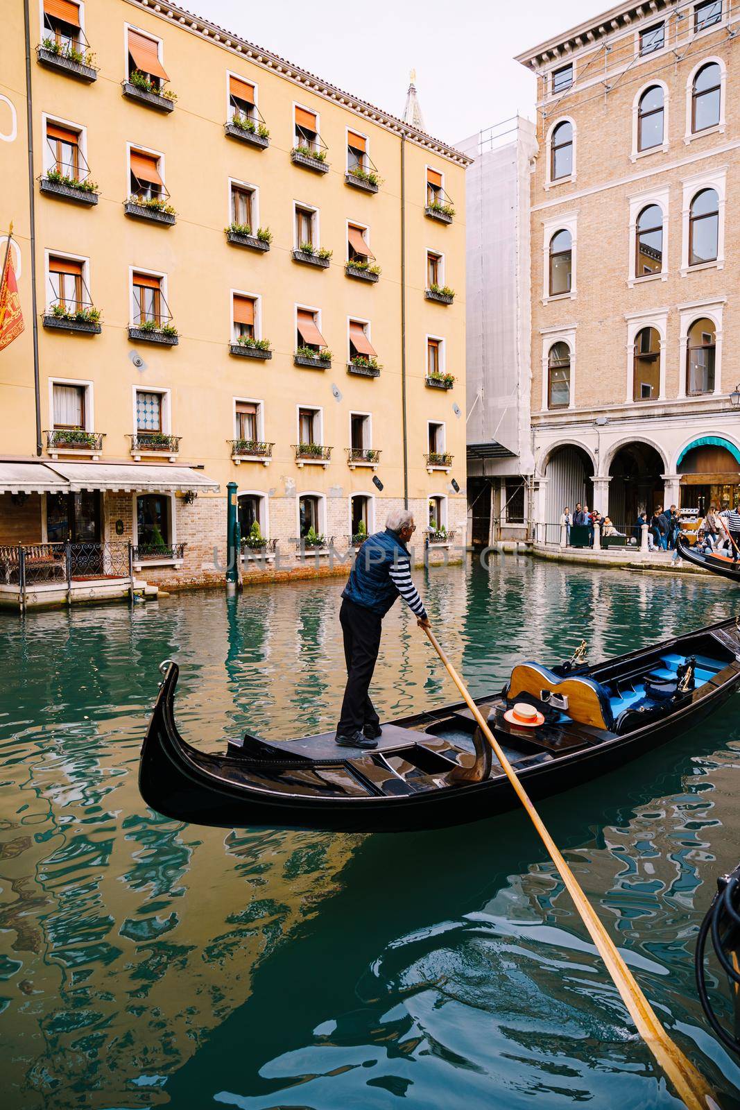 The gondolier rows a paddle in an empty gondola along the canal, against the backdrop of a yellow five-storey building.
