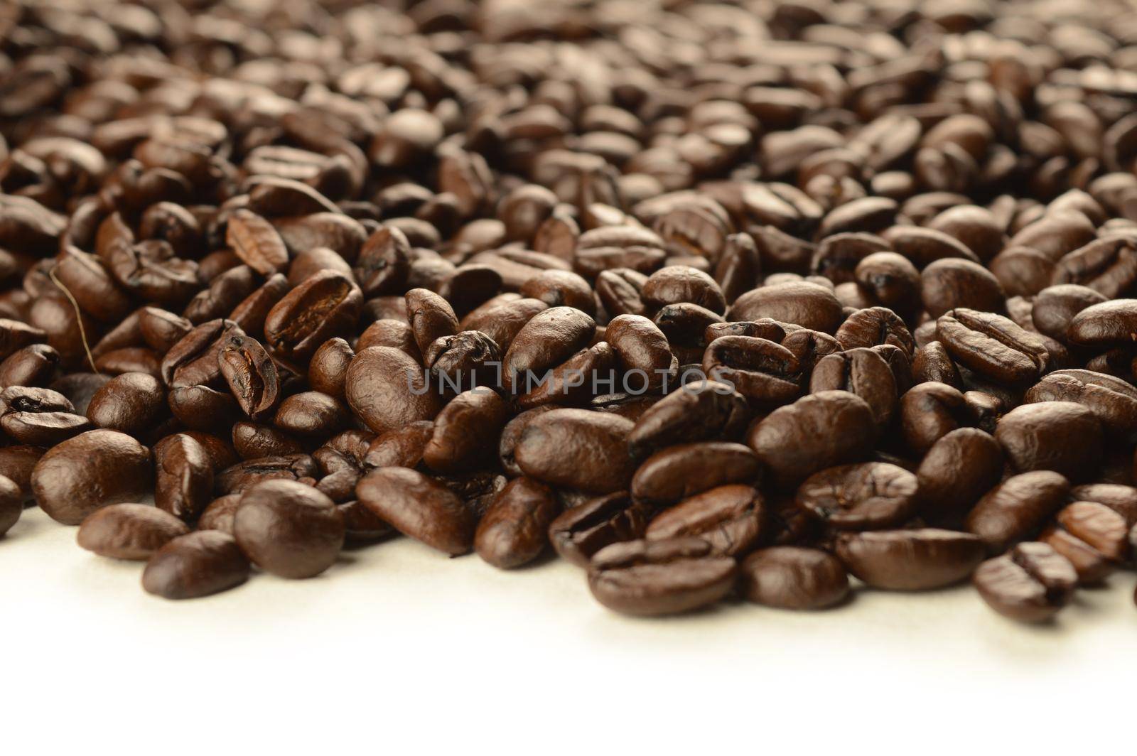 An abundant supply of freshly roasted coffee beans spilling over a clean white background.