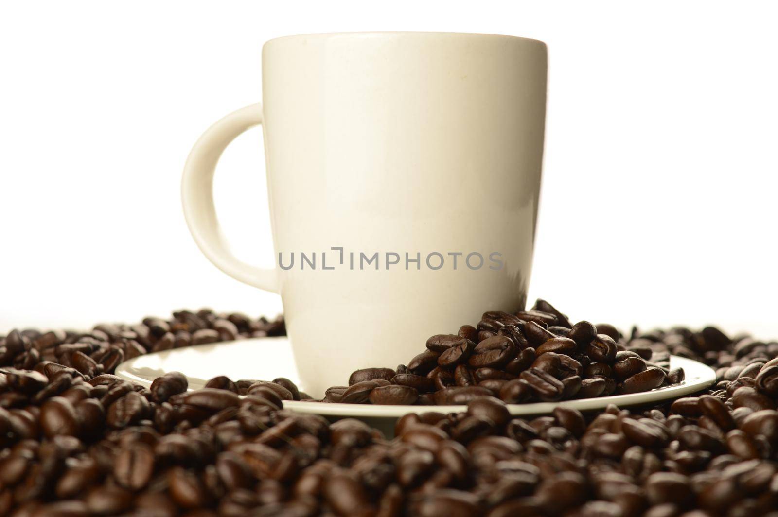 An abundant pile of coffee beans surrounds a white cup and saucer over a clean white background.