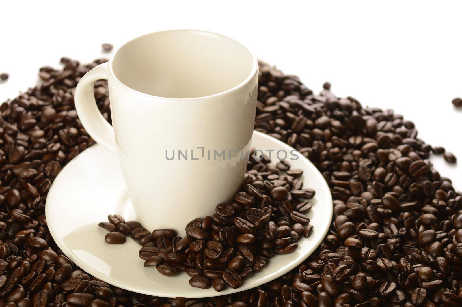 An abundant pile of coffee beans surrounds a white cup and saucer over a clean white background.