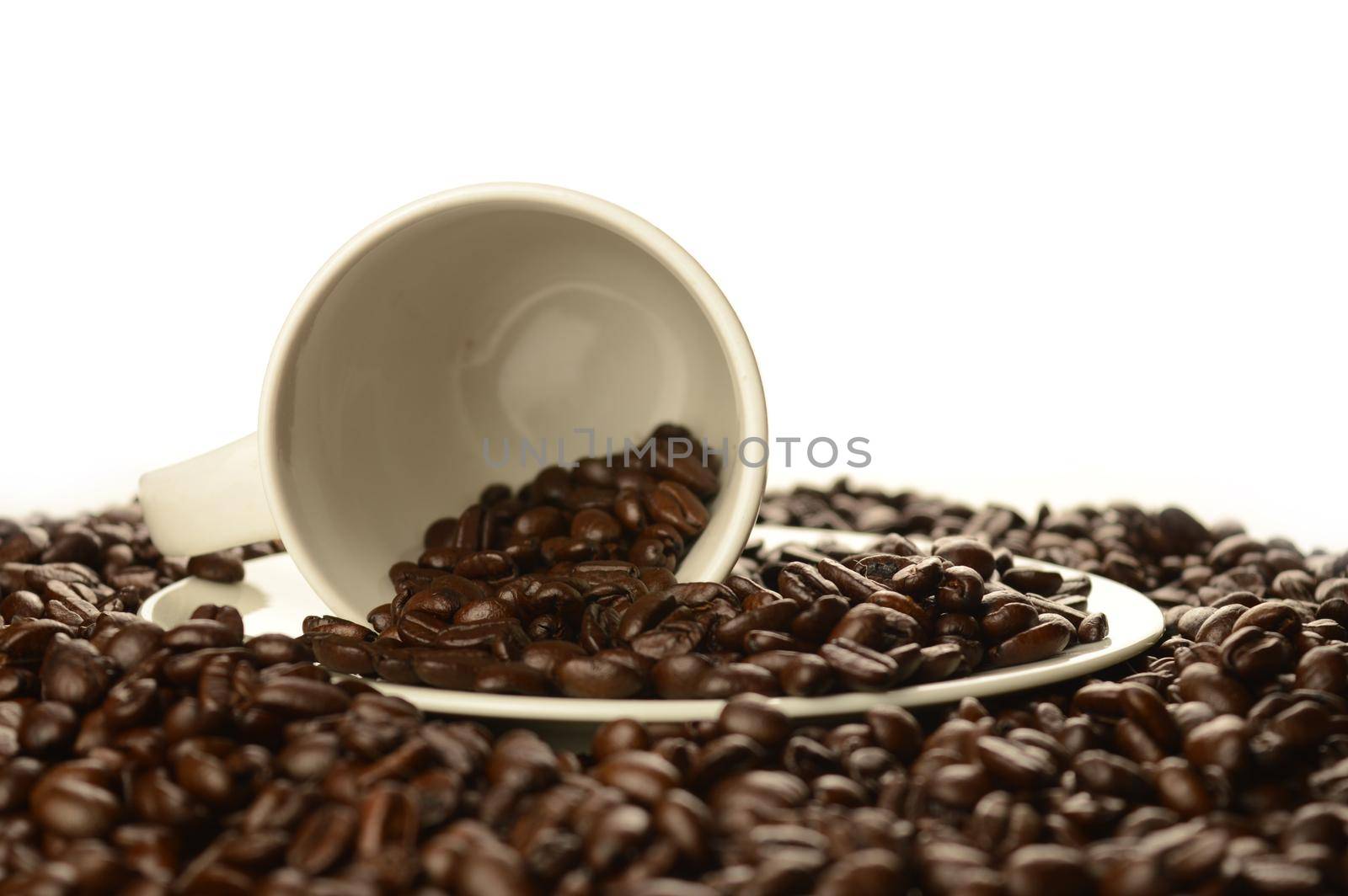 An abundant pile of coffee beans surrounds a white cup and saucer over a clean white background.