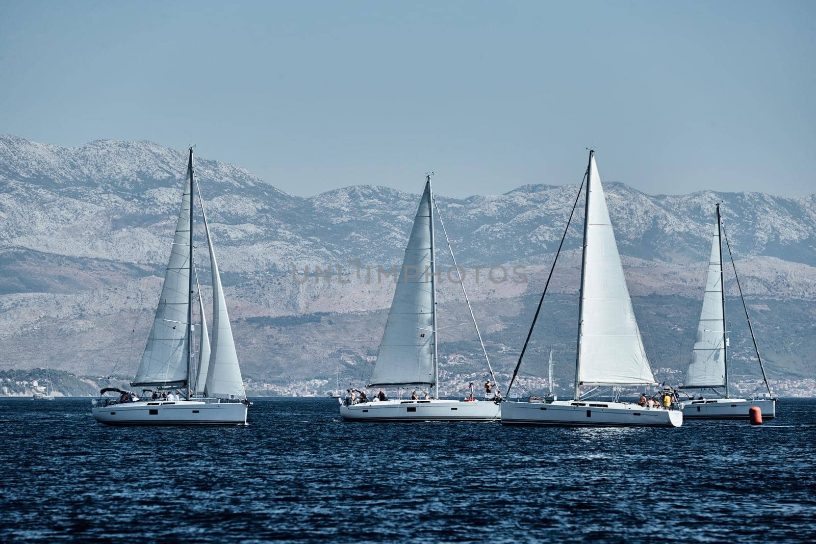 The race of sailboats, a regatta, reflection of sails on water, Intense competition, number of boat is on aft boats, bright colors, island with windmills are on background by vladimirdrozdin