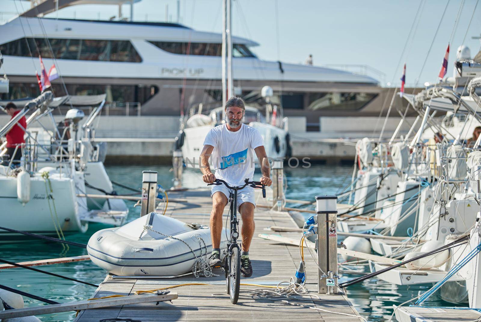 Croatia, Split, 15 September 2019: Brutal participant of a sailing regatta with boats on a background goes by bicycle on a pier, people is waiting for the forthcoming race