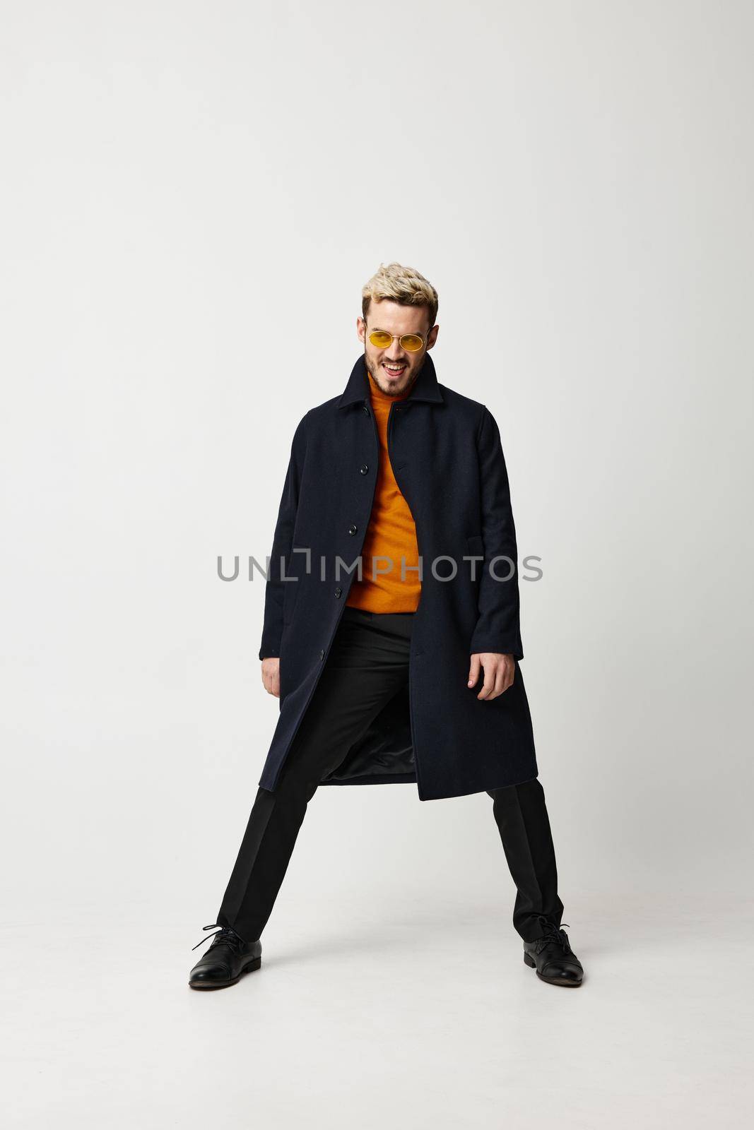 fashionable man in a coat spread his legs on a light background and orange sweater pants shoes. High quality photo