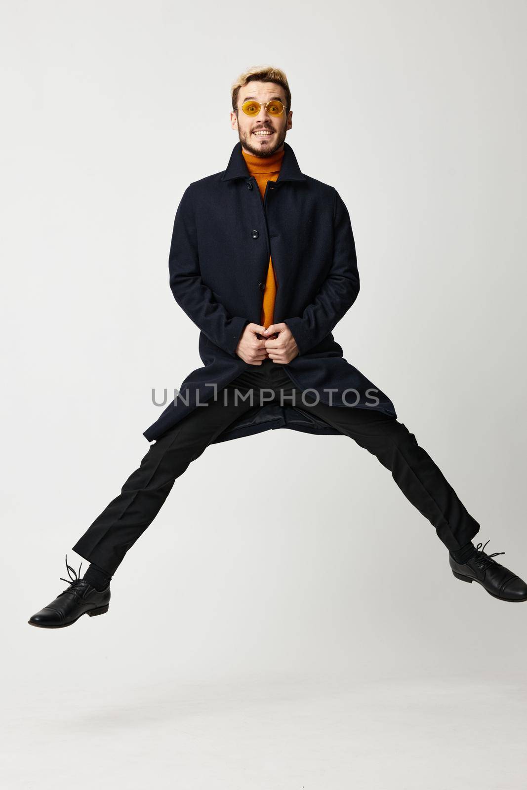 fashionable man in black coat jumped up with legs apart and orange sweater Copy Space. High quality photo