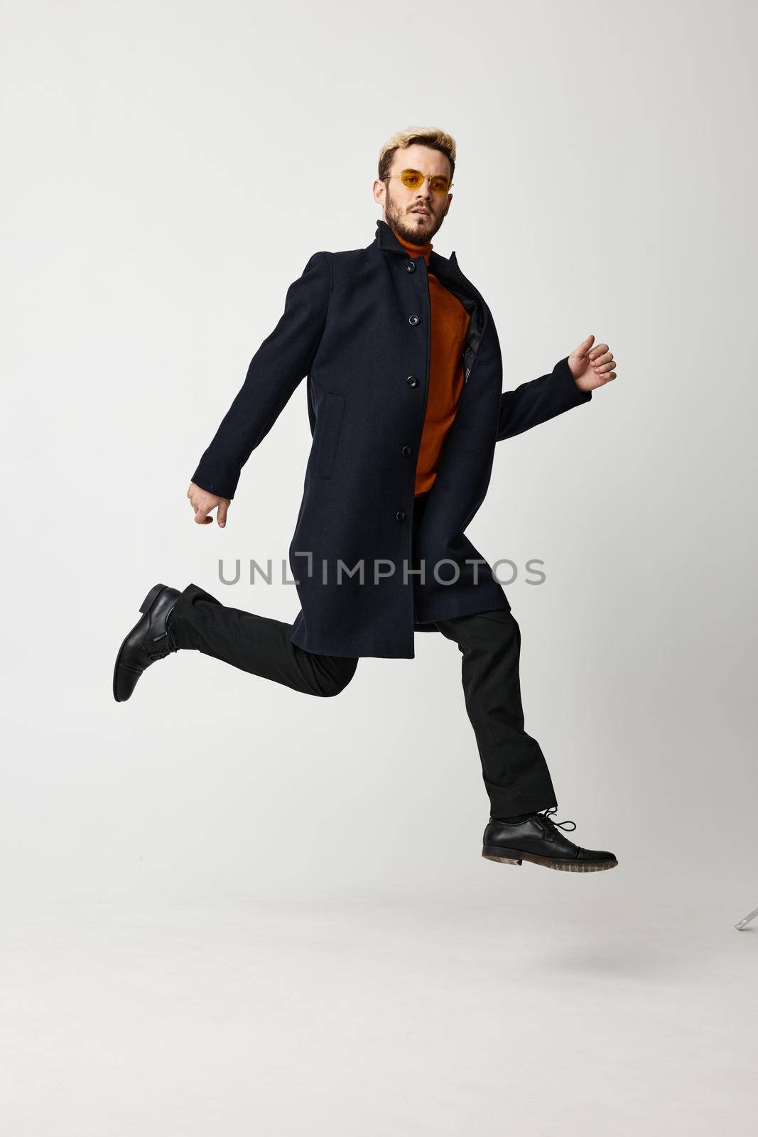 a blond man in a coat jumped up and runs to the side on a light background. High quality photo