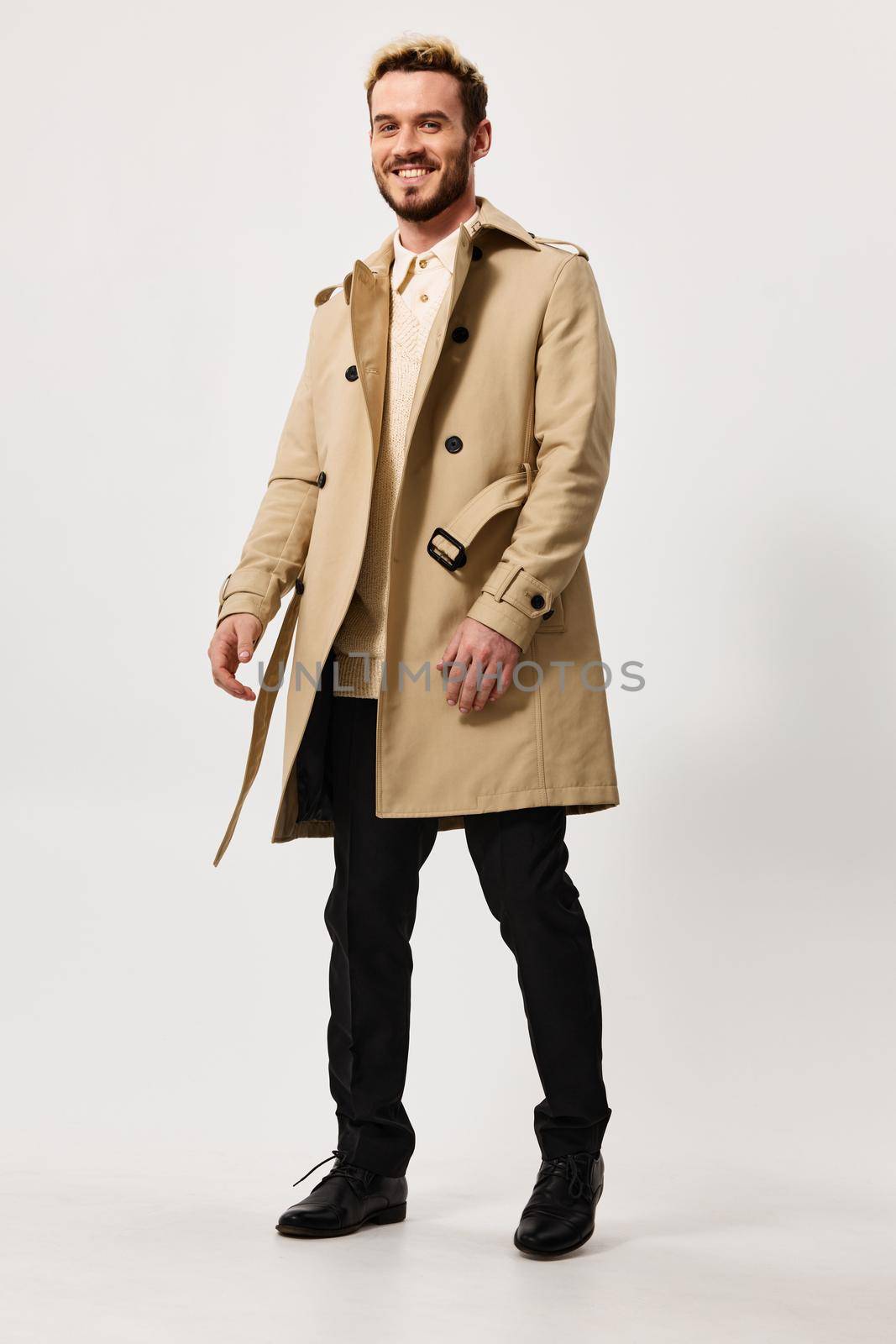 cute guy in beige coat and trousers goes to the side on a light background and fashion style suit by SHOTPRIME