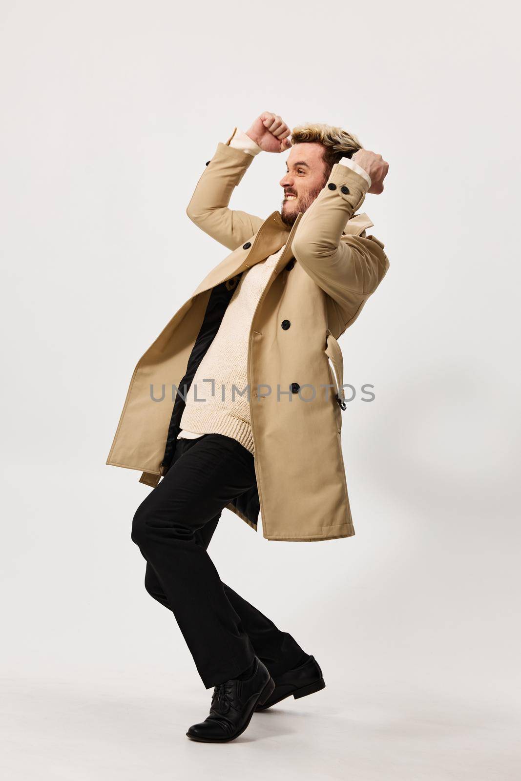 happy man in beige coat and fashionable trousers holds hands in fist success luck fun. High quality photo
